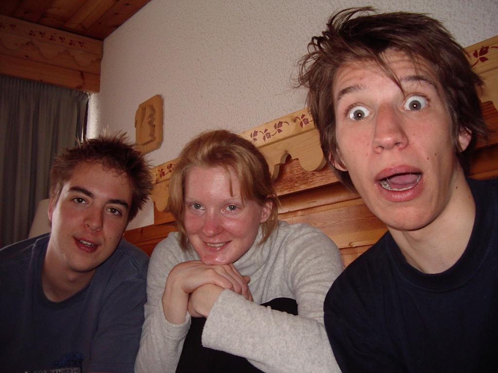 Three young people sitting close together, smiling and making playful expressions while looking at the camera.