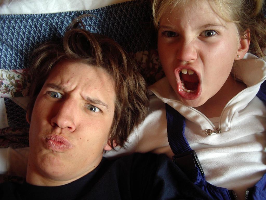 Two people making playful facial expressions; one looks serious, while the other has their mouth open as if shouting.