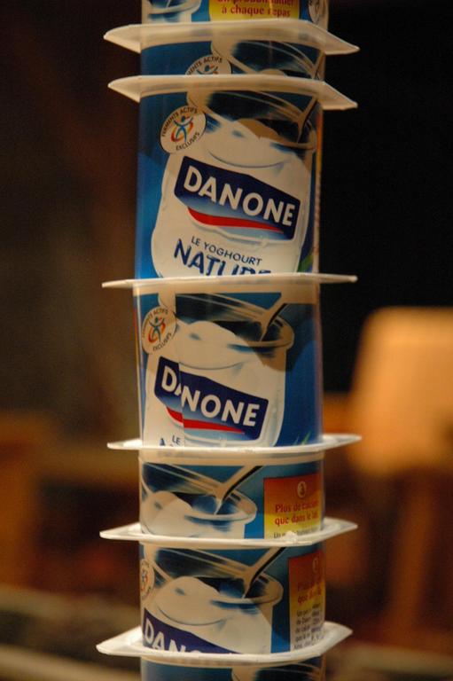 A tall stack of Danone yogurt containers balanced on top of each other.