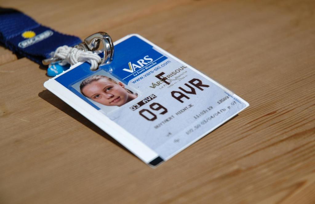 A ski pass with a photo ID and lanyard lies on a wooden surface.