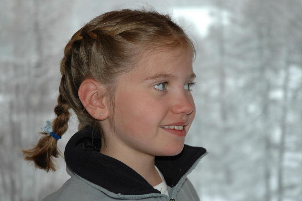 A young girl with braided hair and a winter jacket looks to the side with a slight smile.