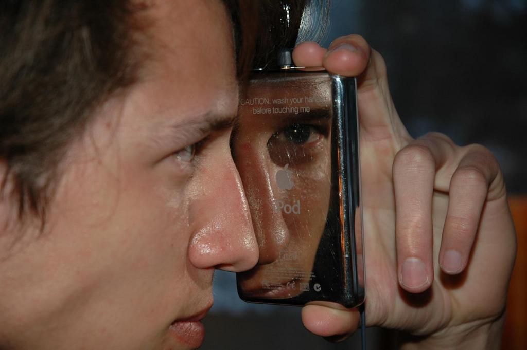 A person holds a reflective iPod close to their face, showing their reflection on its shiny surface.
