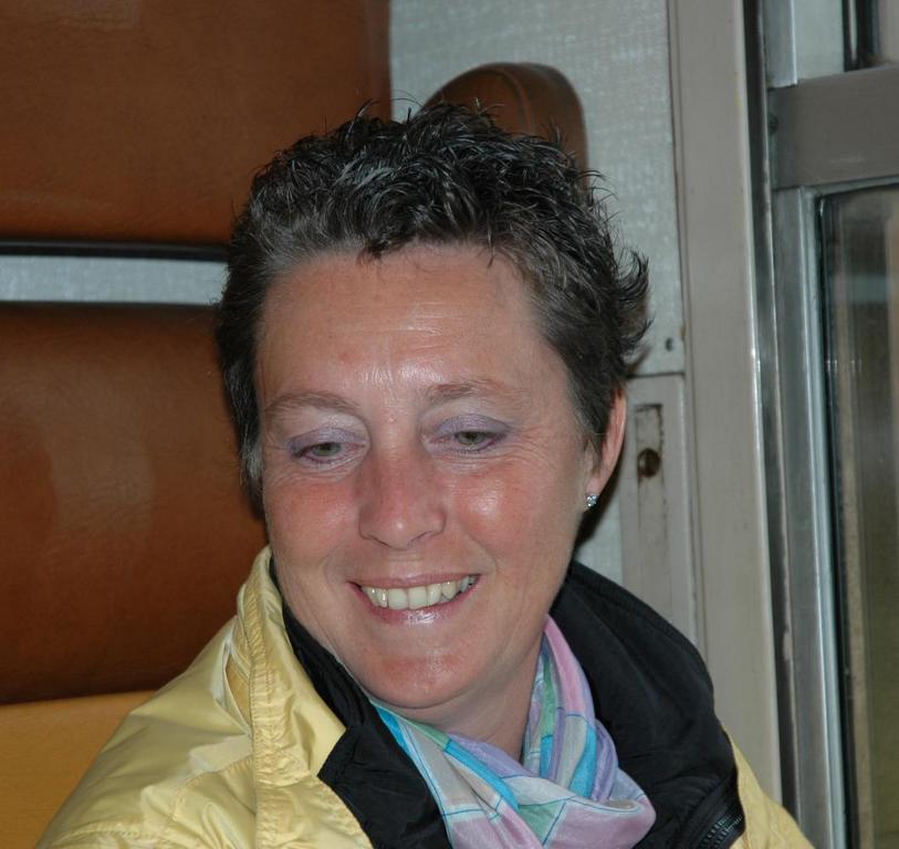A person with short hair and a scarf smiles while sitting near a window in a vehicle.
