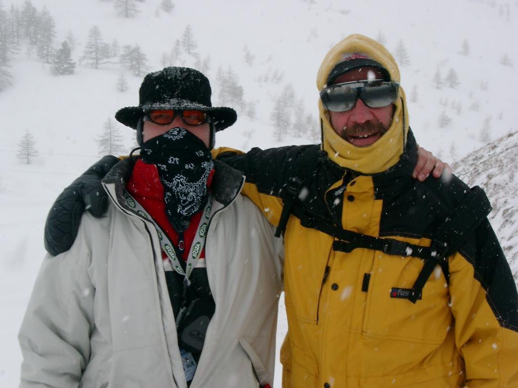 Two people in winter gear stand close together in a snowy landscape, smiling and posing for the camera.