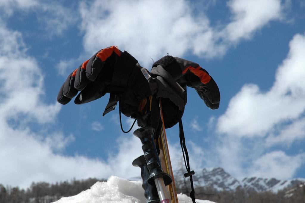 A pair of gloves rest on ski poles stuck in the snow, with a mountain and sky in the background.