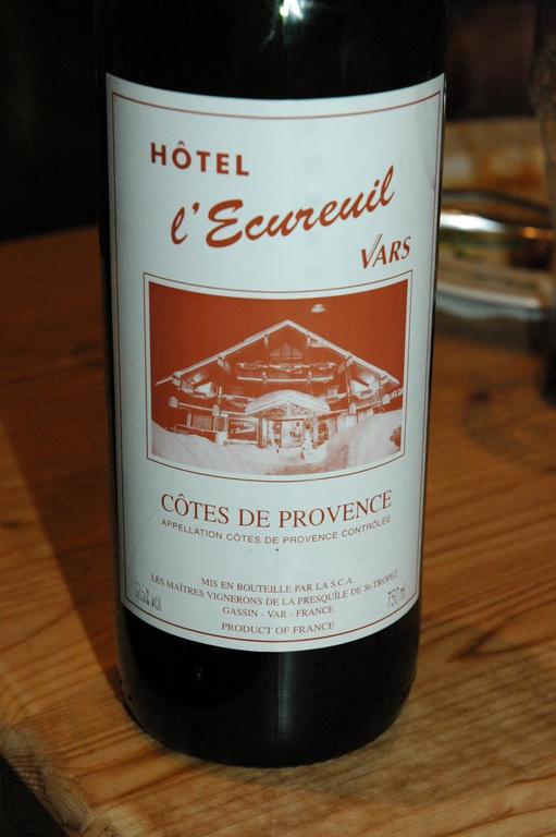 A bottle of Côtes de Provence wine with a label featuring Hôtel l'Ecureuil in Vars, placed on a table.