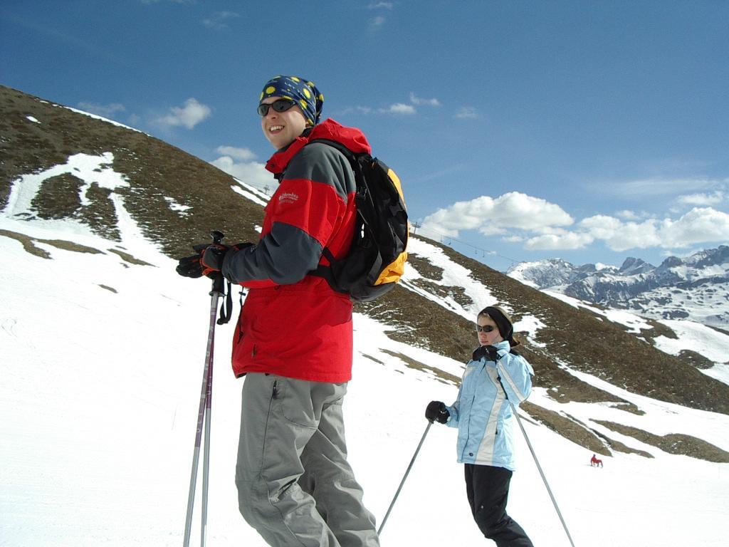 Two people skiing on a snowy mountain, wearing winter jackets and carrying ski poles.