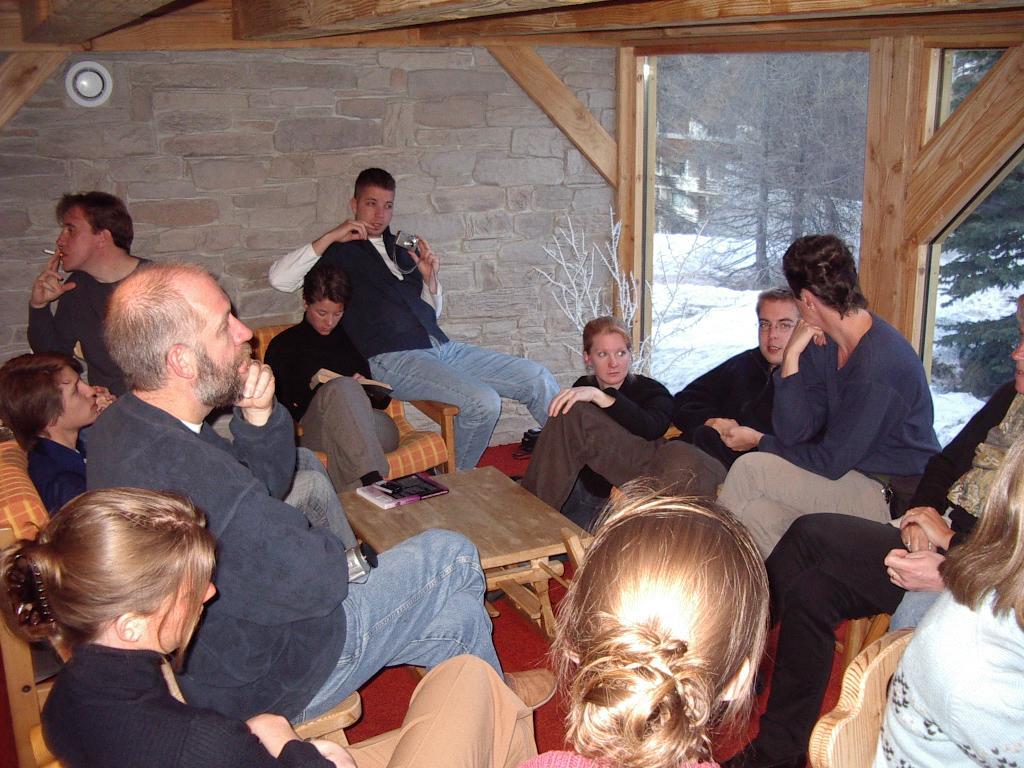 A group of people sits in a cozy room, talking and relaxing near a window with a snowy view.