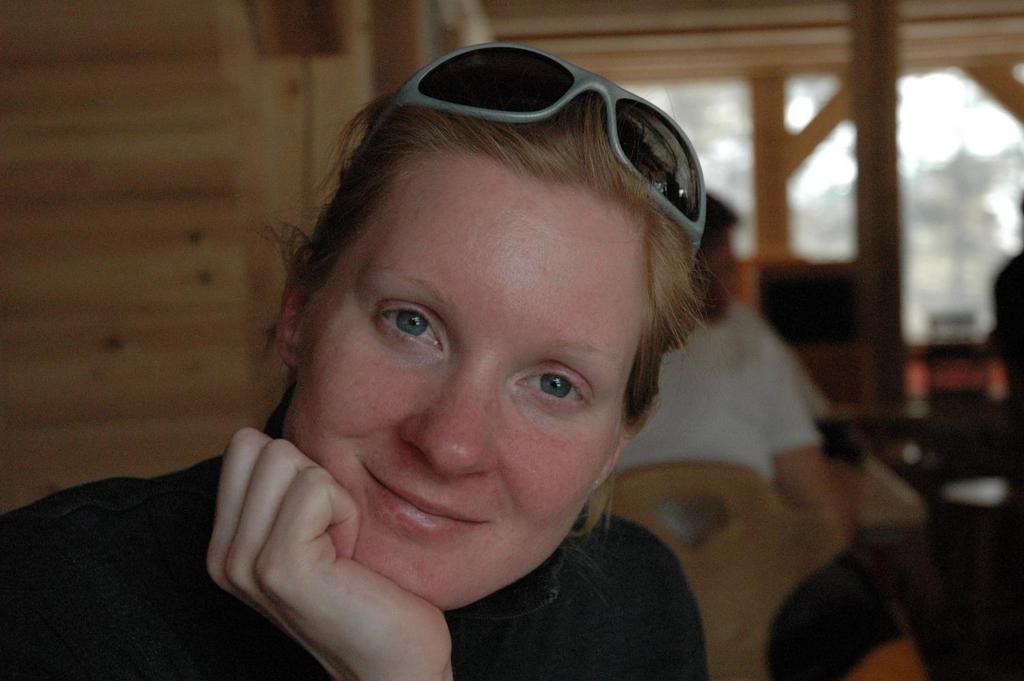 A person with sunglasses on their head rests their chin on their hand and looks at the camera.