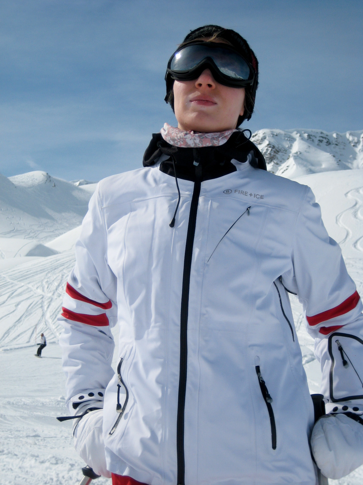 A person wearing a white ski jacket and goggles stands in a snowy mountain landscape.