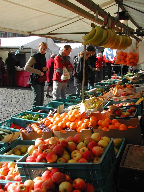 People shopping for fresh fruits and vegetables at an outdoor market with crates of apples, oranges, and bananas.