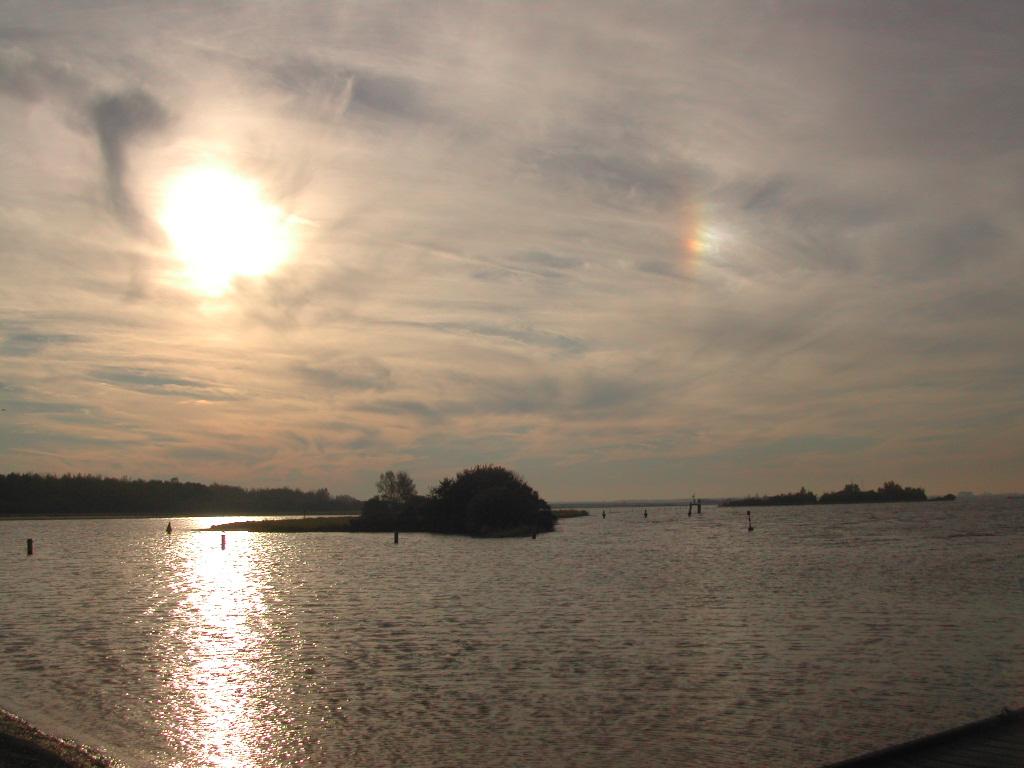 The sun reflects on the calm water of Veerse Meer, with small islands and buoys visible in the distance.