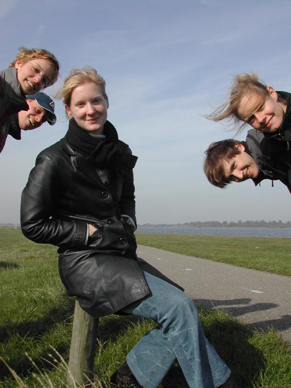 A person sits on a wooden post while four others playfully lean into the frame, smiling.