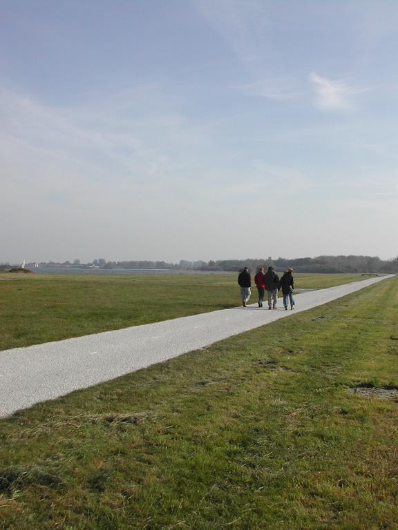 Four people walk along a paved path through a grassy field under a clear sky.