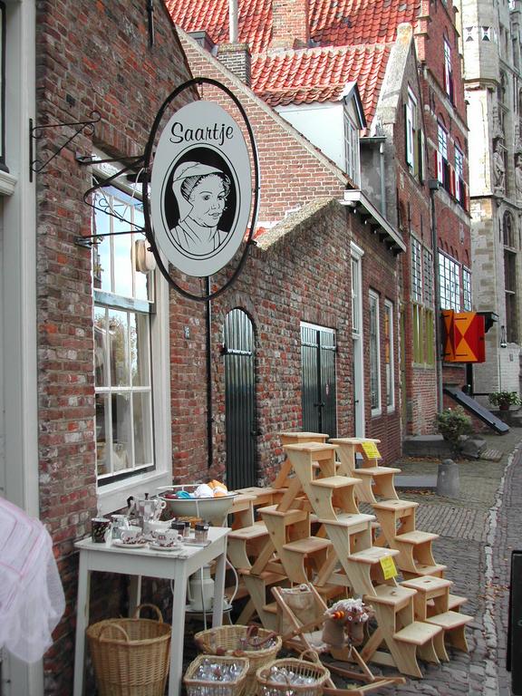 A small shop with a sign reading "Saartje" displays wooden stools, baskets, and ceramics on a cobblestone street.