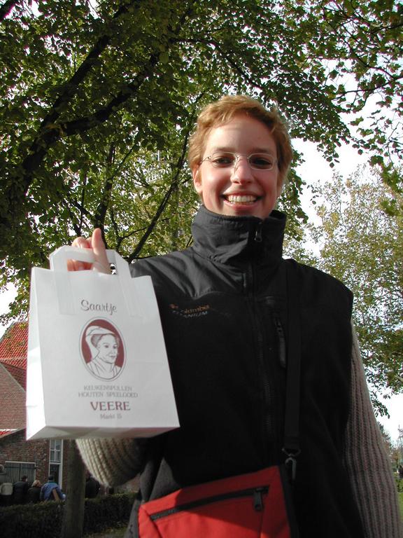 A smiling person holds up a white shopping bag with a logo and text from a store in Veere.