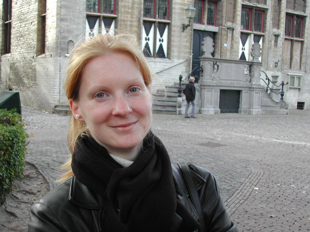 A woman with red hair and a black scarf smiles at the camera in front of a historic building.