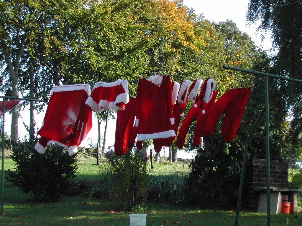 Santa Claus costumes hanging on a clothesline outdoors, drying in the sunlight.