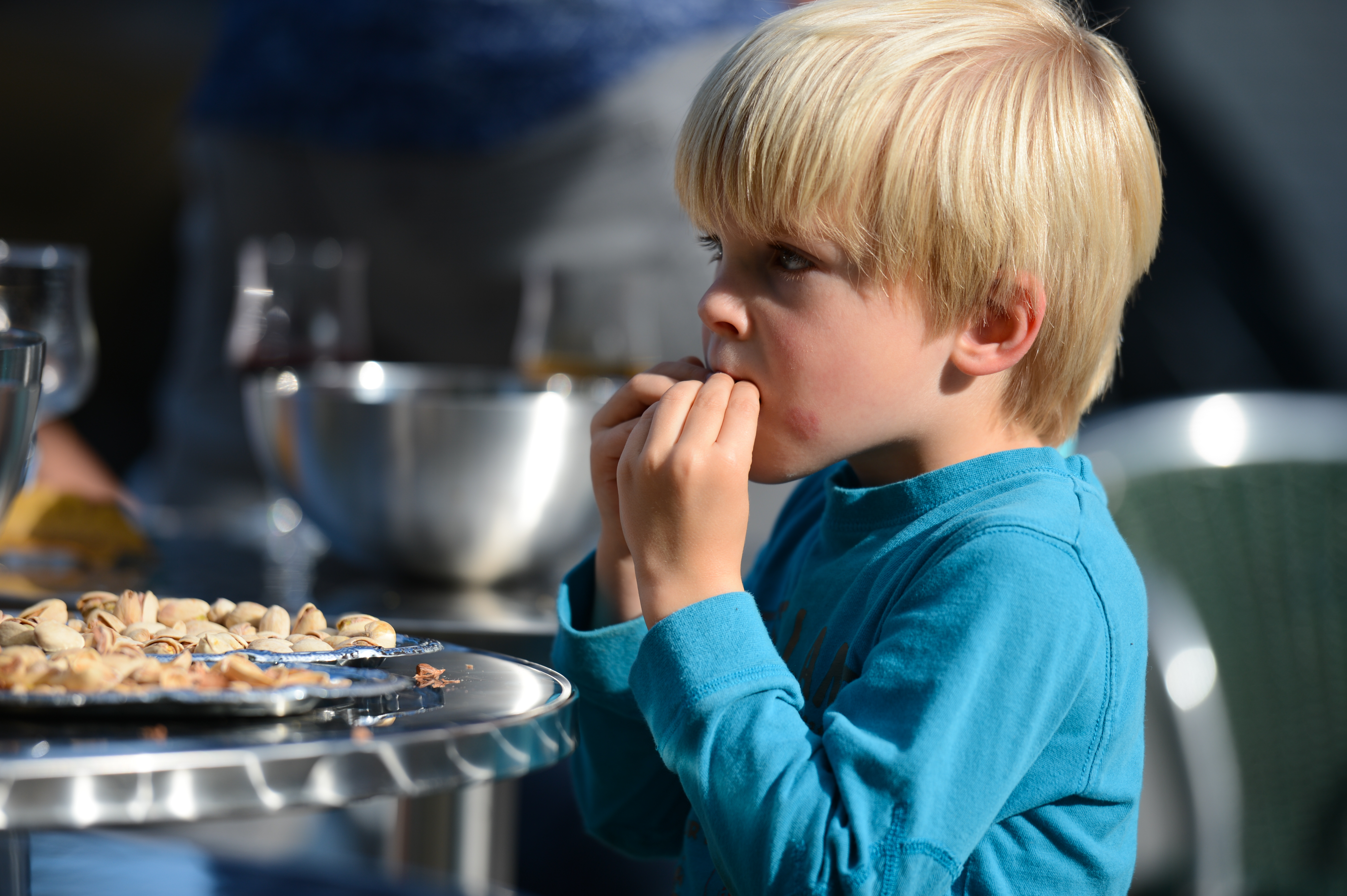 A young boy in a blue shirt eats pistachios at an outdoor table during a family gathering.