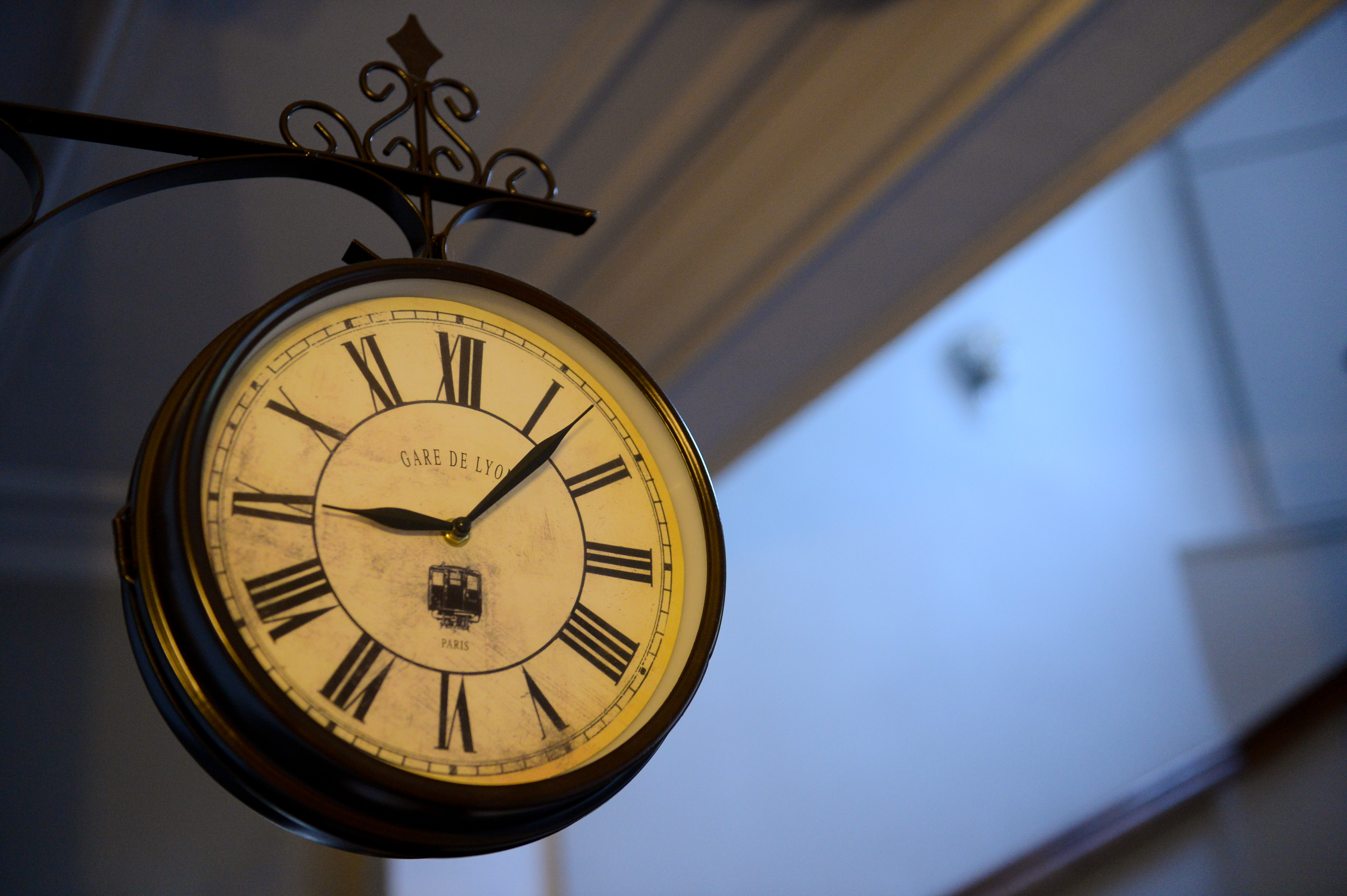 A vintage-style clock with Roman numerals hangs on a metal bracket near a staircase, showing the time 9:08.