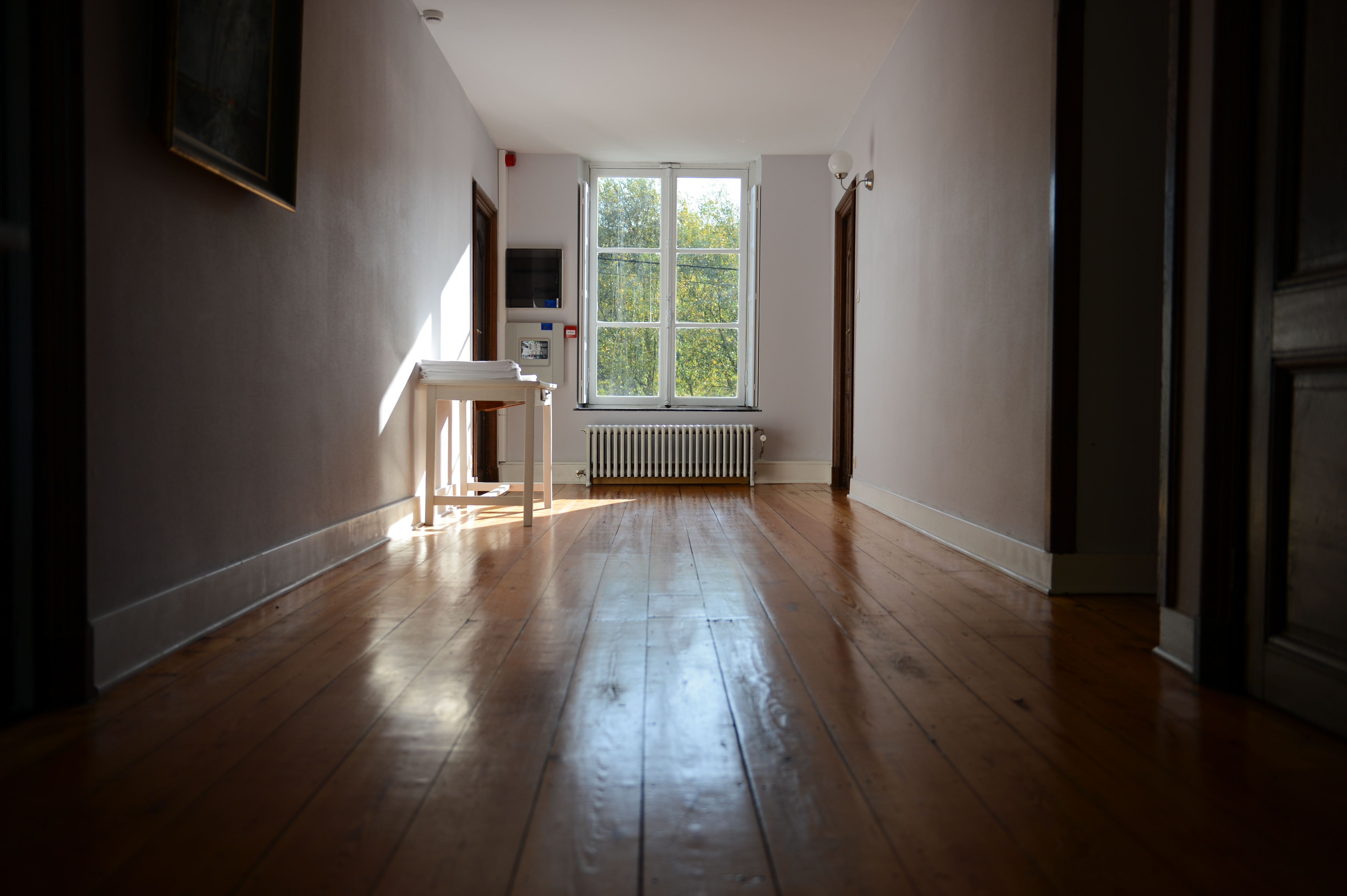 A quiet hallway with wooden floors, a small table, and a window letting in natural light.