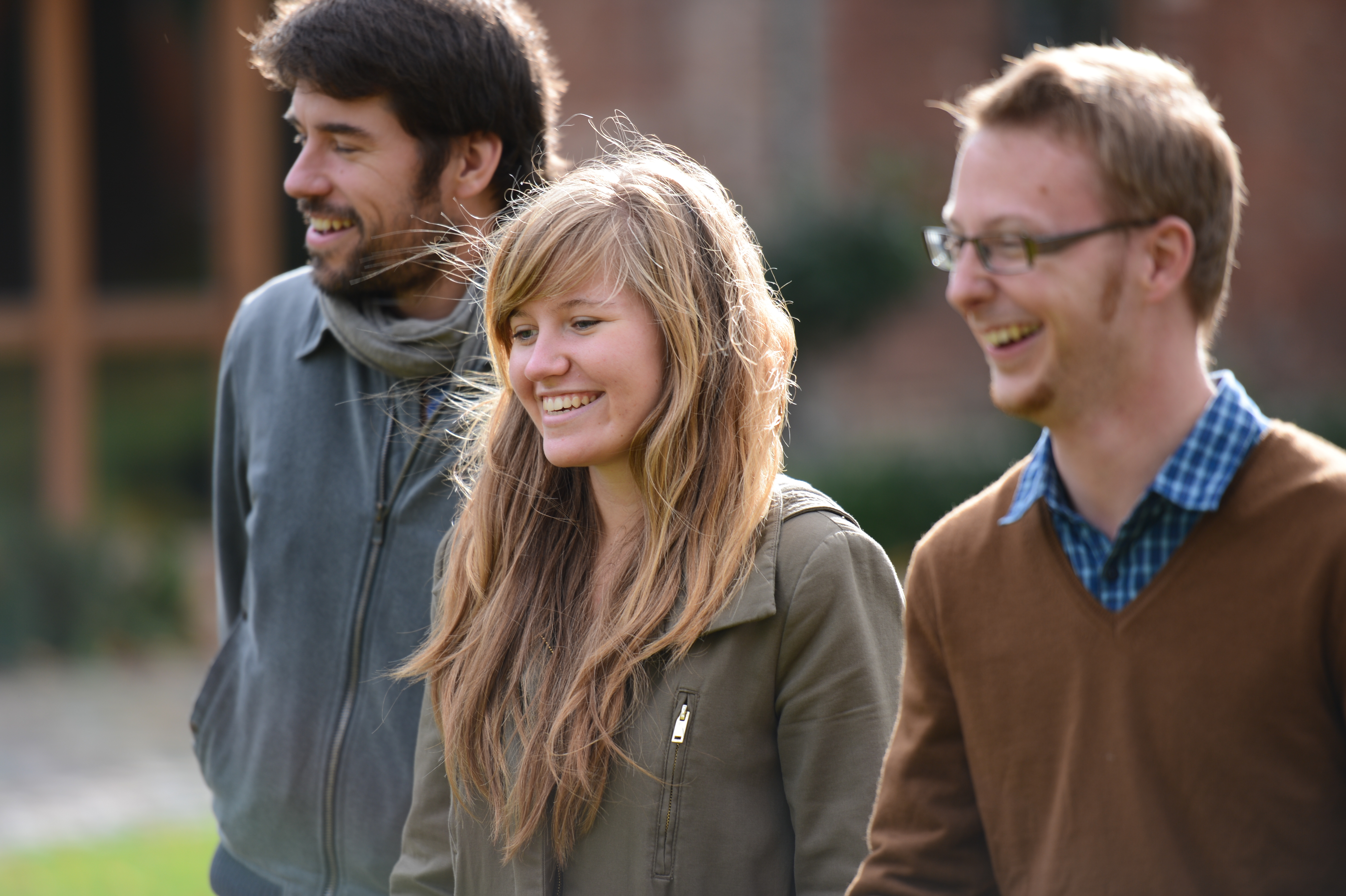 Three people walk outdoors, smiling and laughing together during a family weekend gathering.