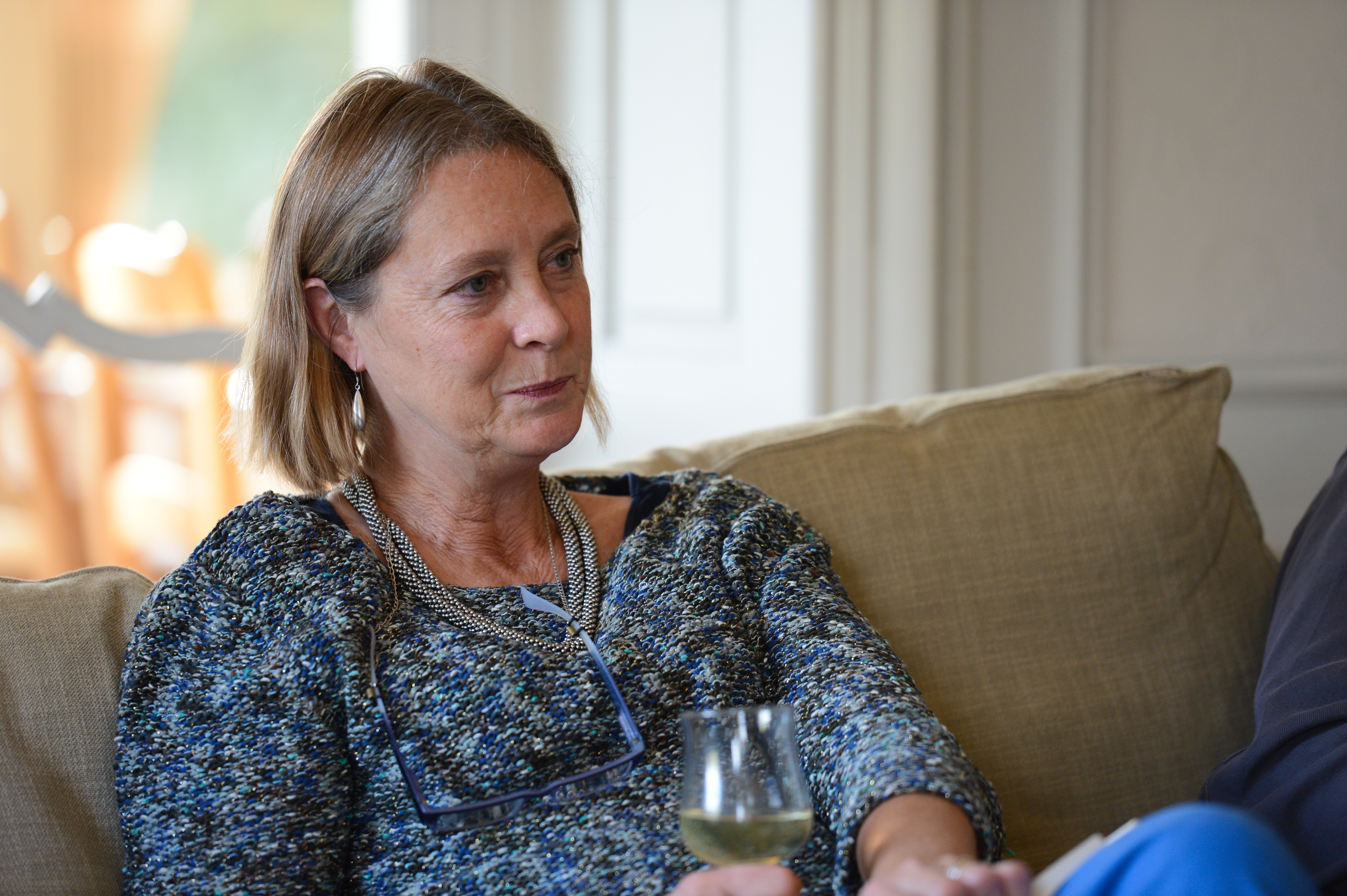 A woman sits on a couch, holding a glass of wine and engaged in conversation.