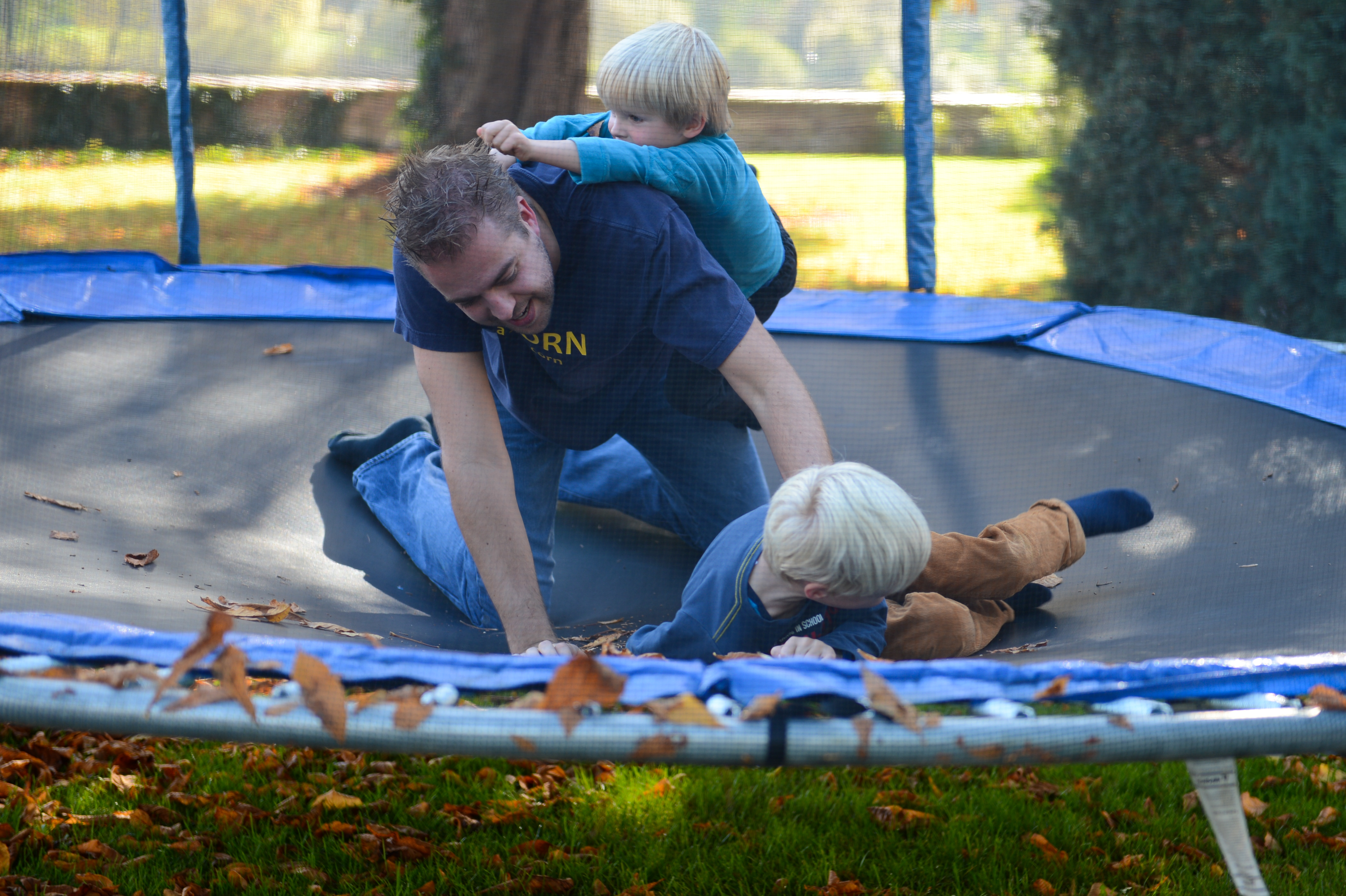 A man and two children play on a trampoline, laughing and climbing on each other during a family weekend.