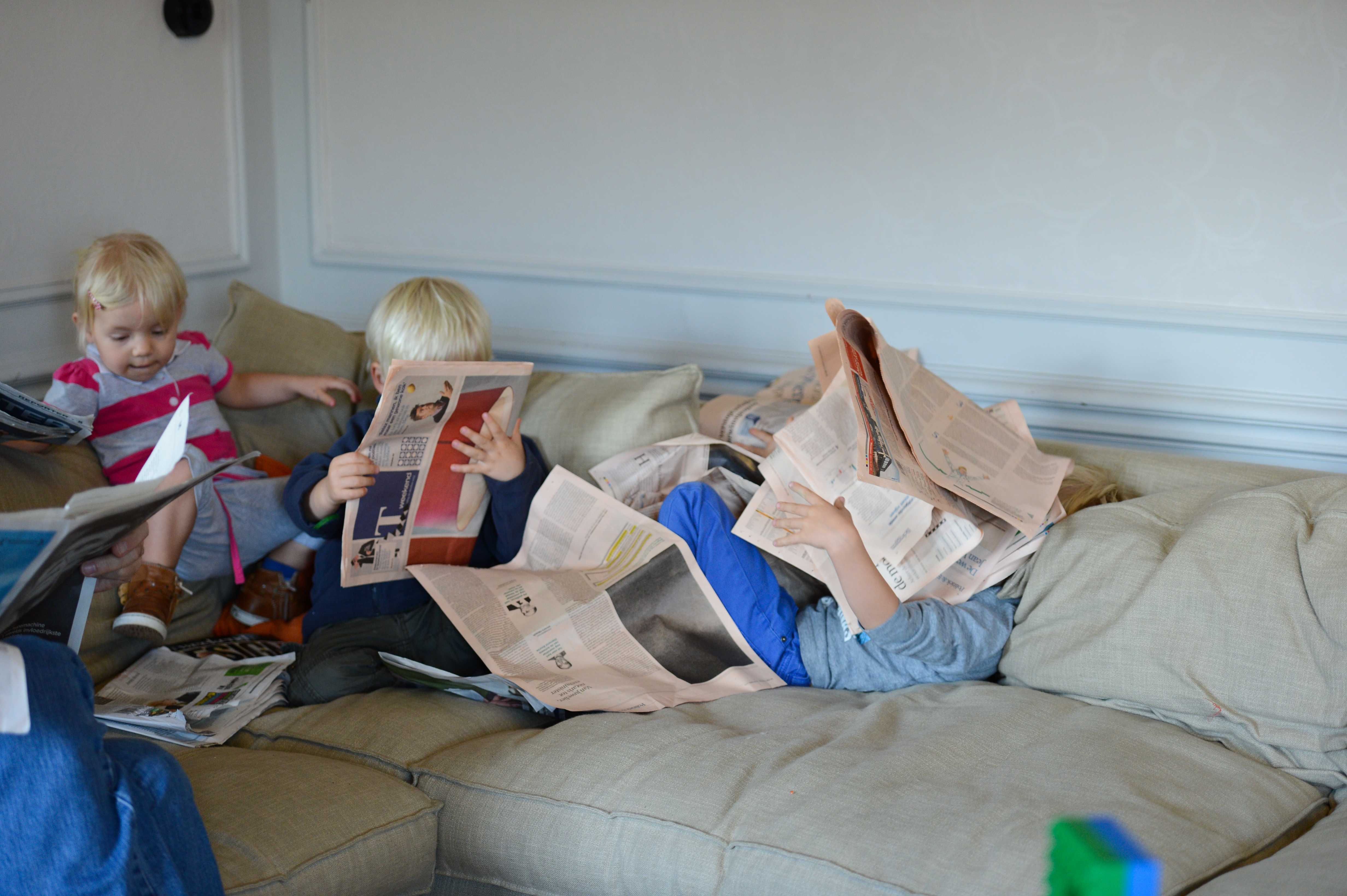 Children sitting on a couch, holding and playing with newspapers.