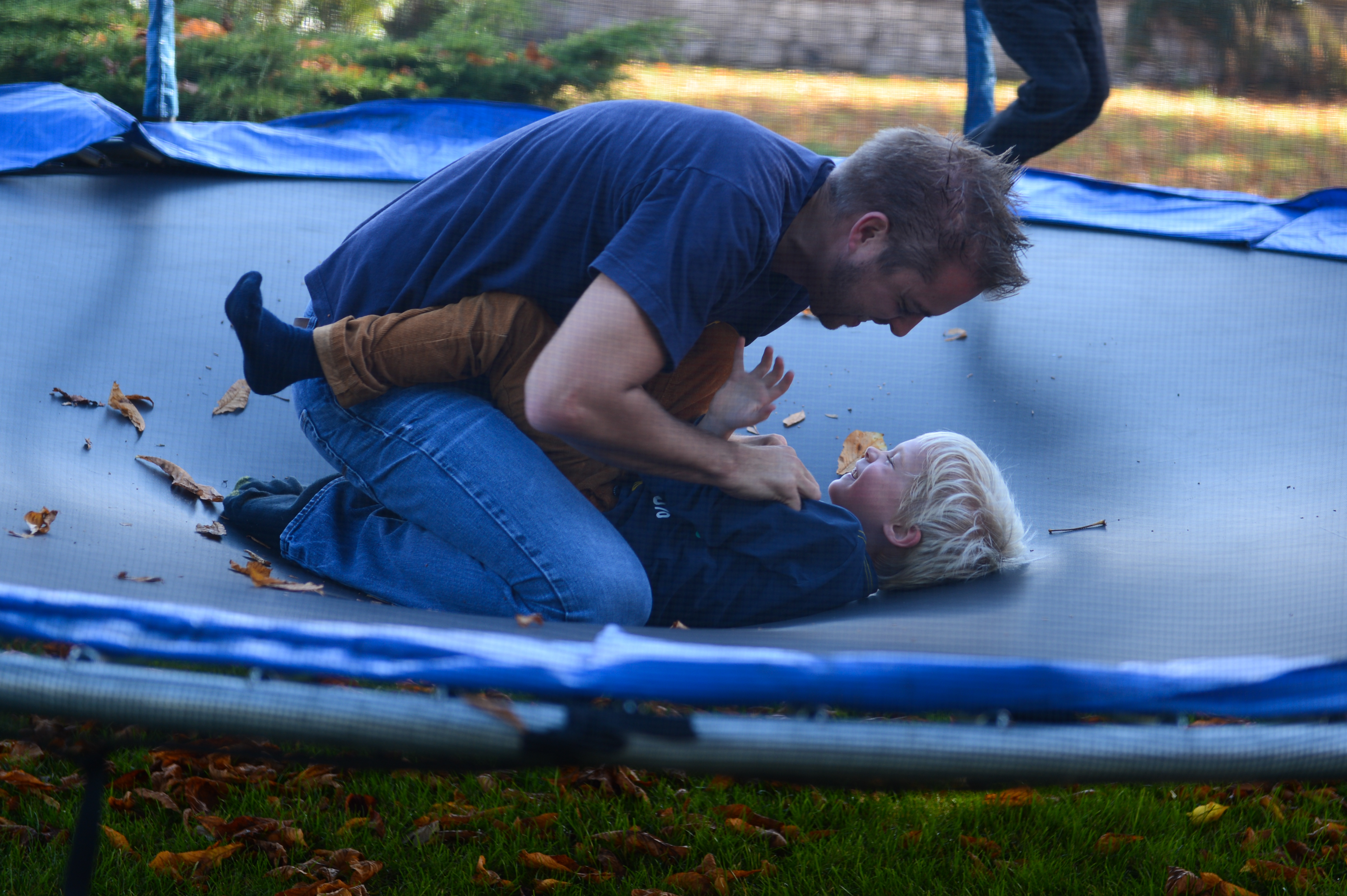 A man and a child laugh while playing together on a trampoline during a family weekend.