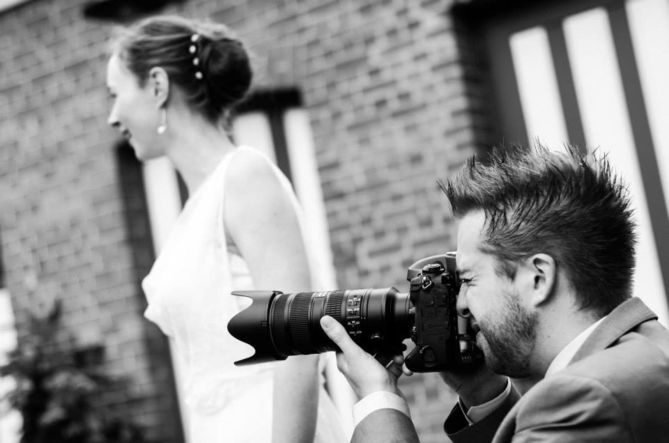 A photographer in a suit takes a close-up shot of a bride walking past in her wedding dress.