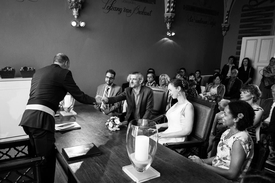 A man in a suit shakes hands with an officiant at a wedding ceremony, with guests watching.