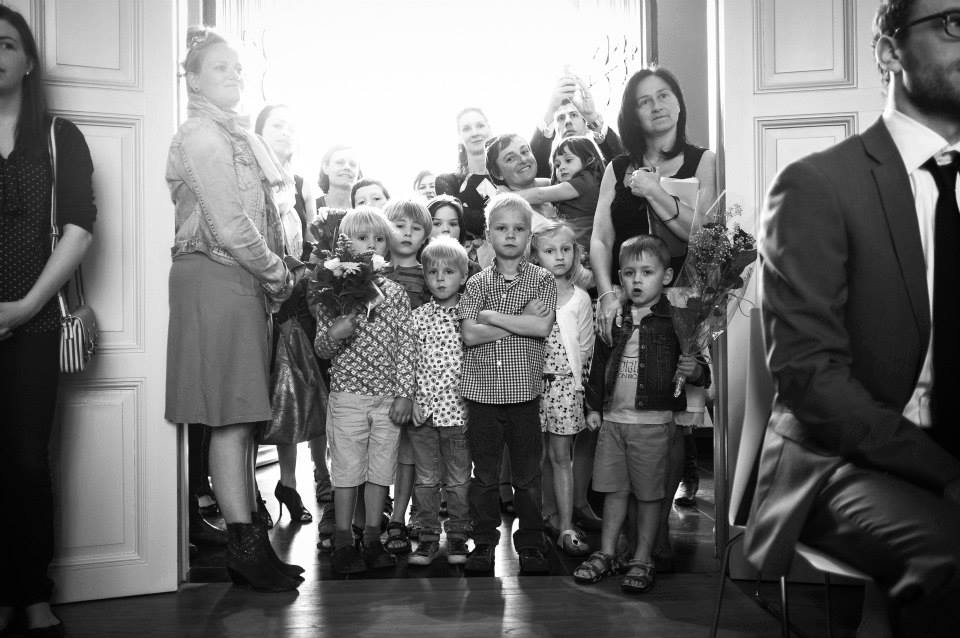 A group of children and adults stand in a doorway, watching the wedding ceremony, some holding flowers.