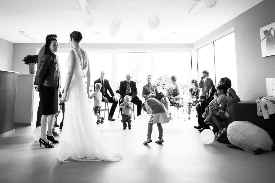 A bride in a wedding dress stands with a woman, while guests and children interact in the background.