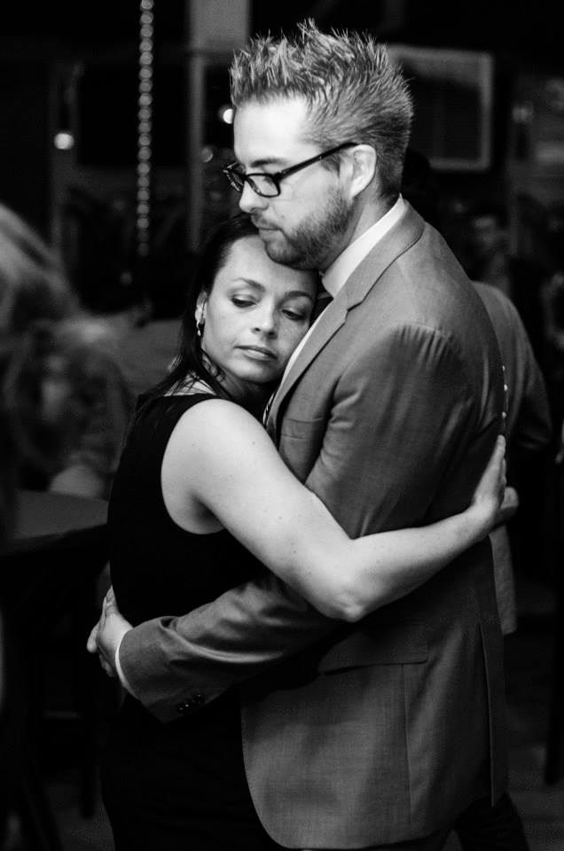 A couple embraces closely on the dance floor, with the woman resting her head on the man's chest.