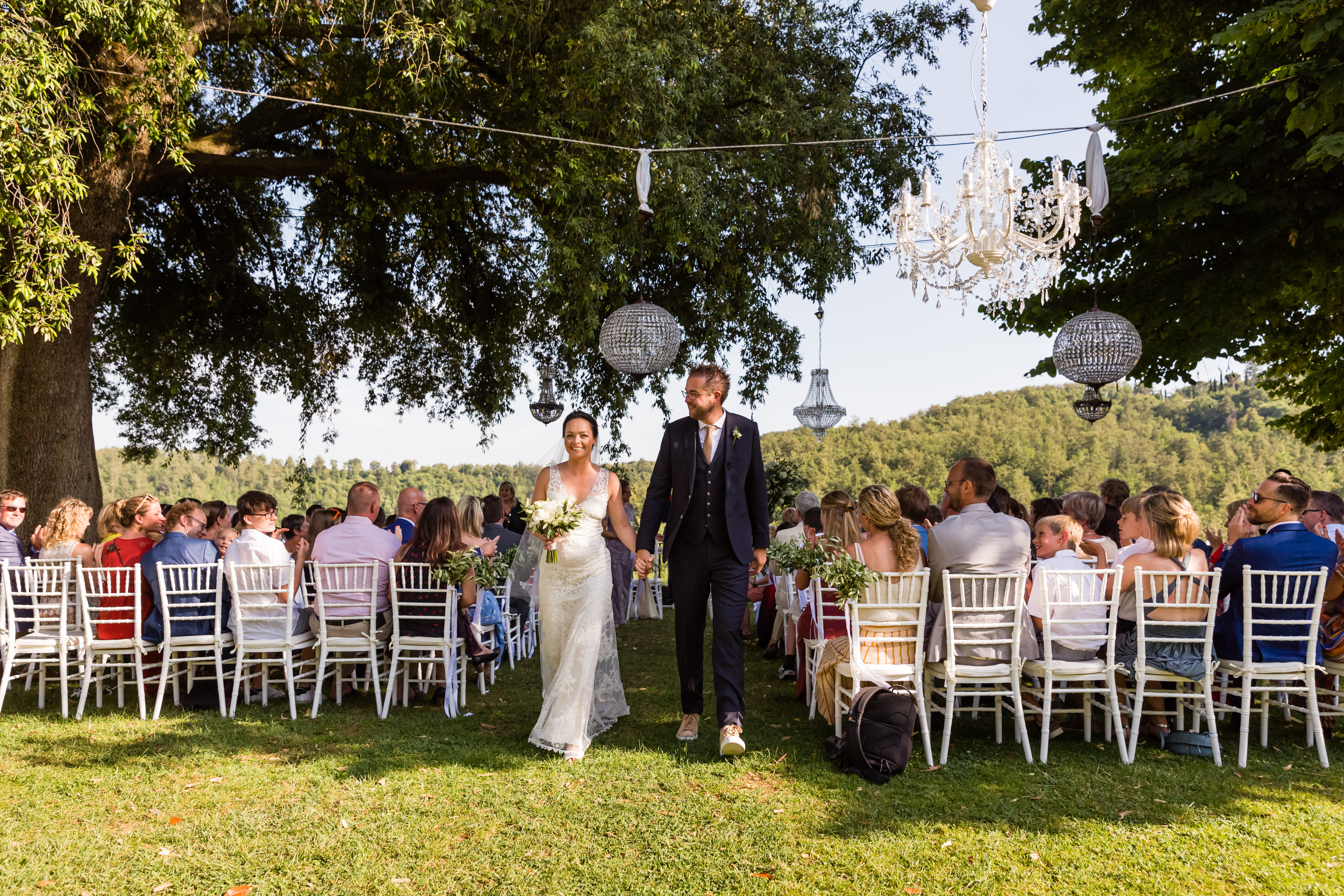 The bride and groom walk hand in hand down the aisle, smiling, as guests watch and celebrate their wedding.