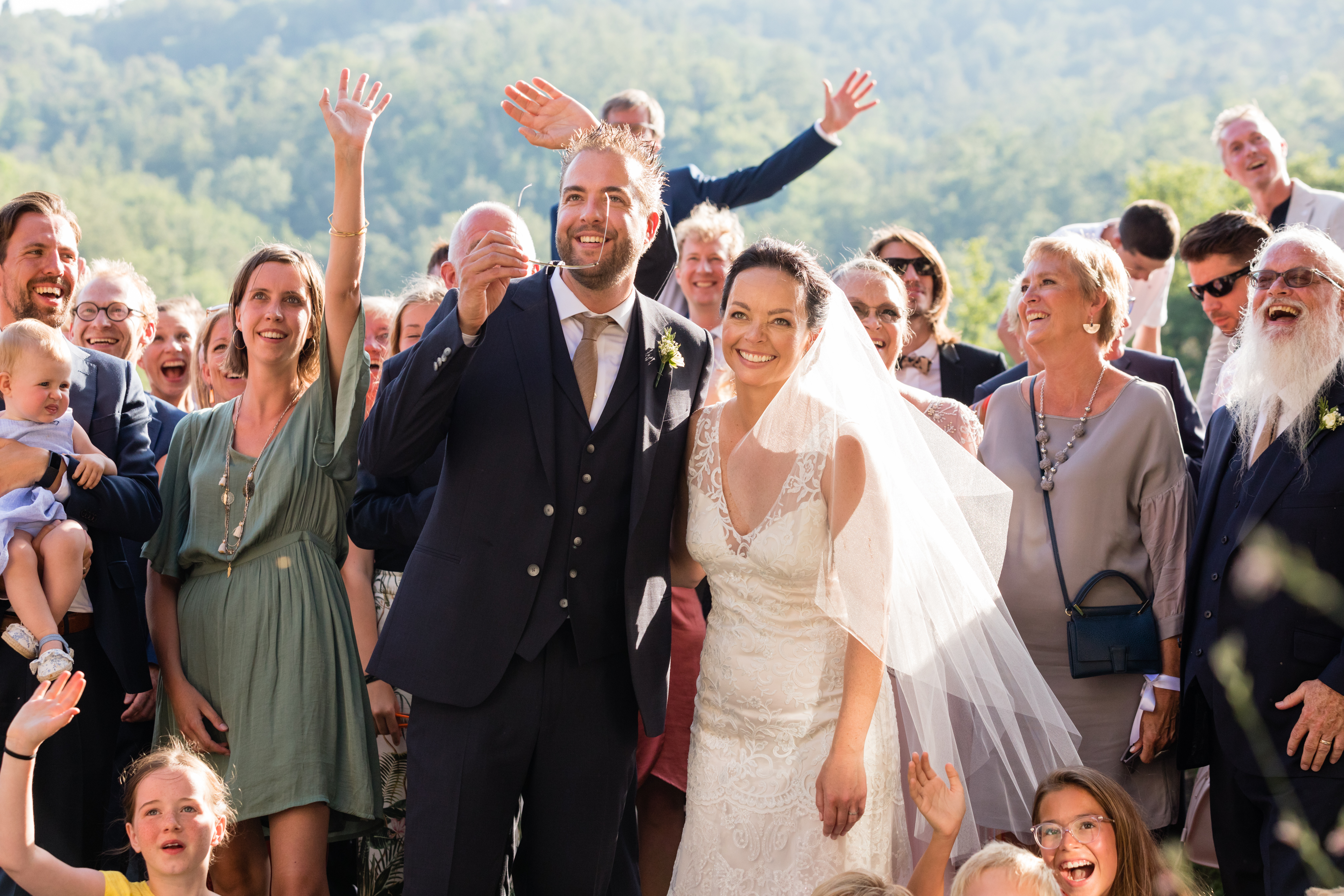 The bride and groom smile joyfully, surrounded by cheering family and friends during their wedding ceremony.