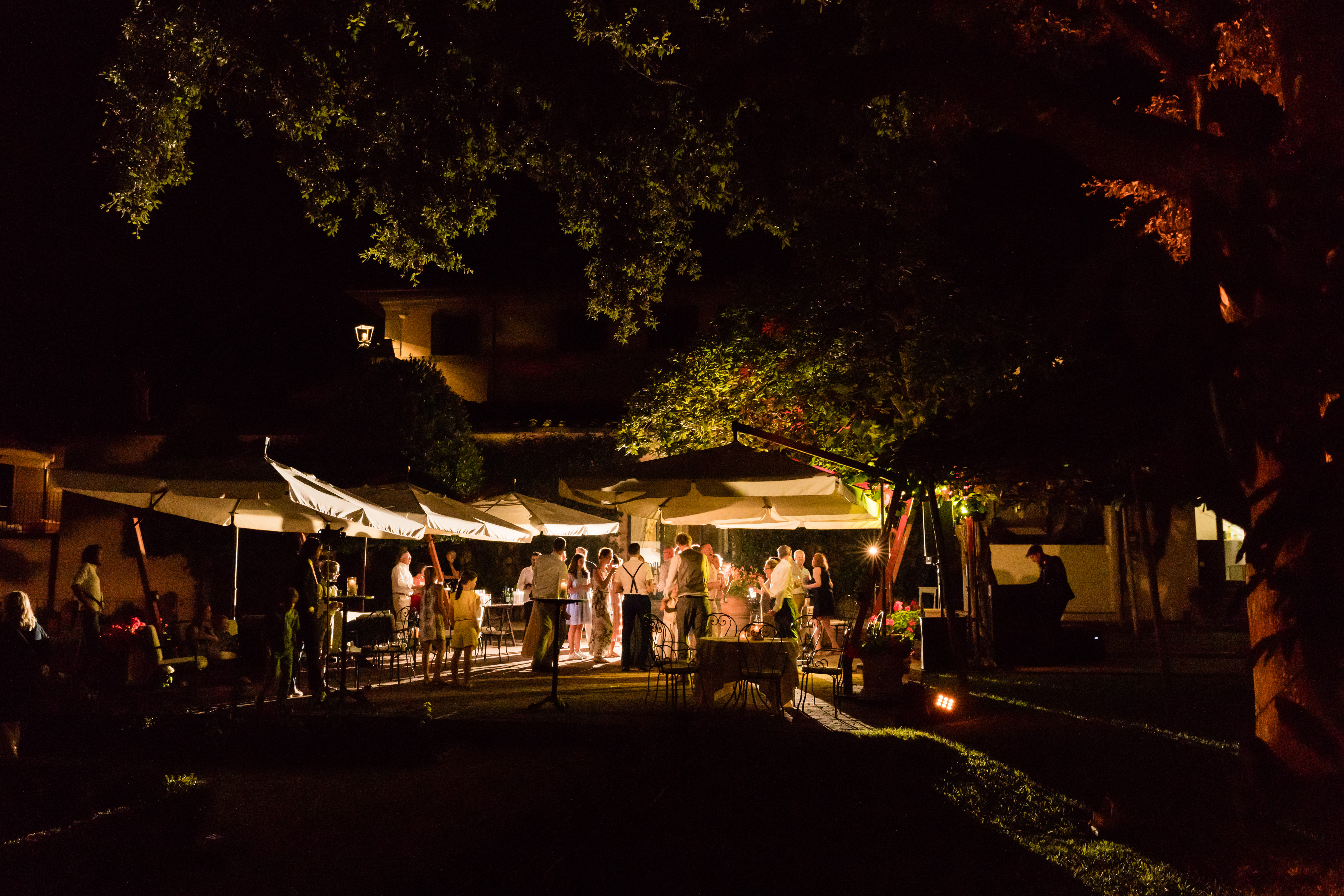 Wedding guests dancing and socializing under outdoor lights at night, with a live musician performing nearby.