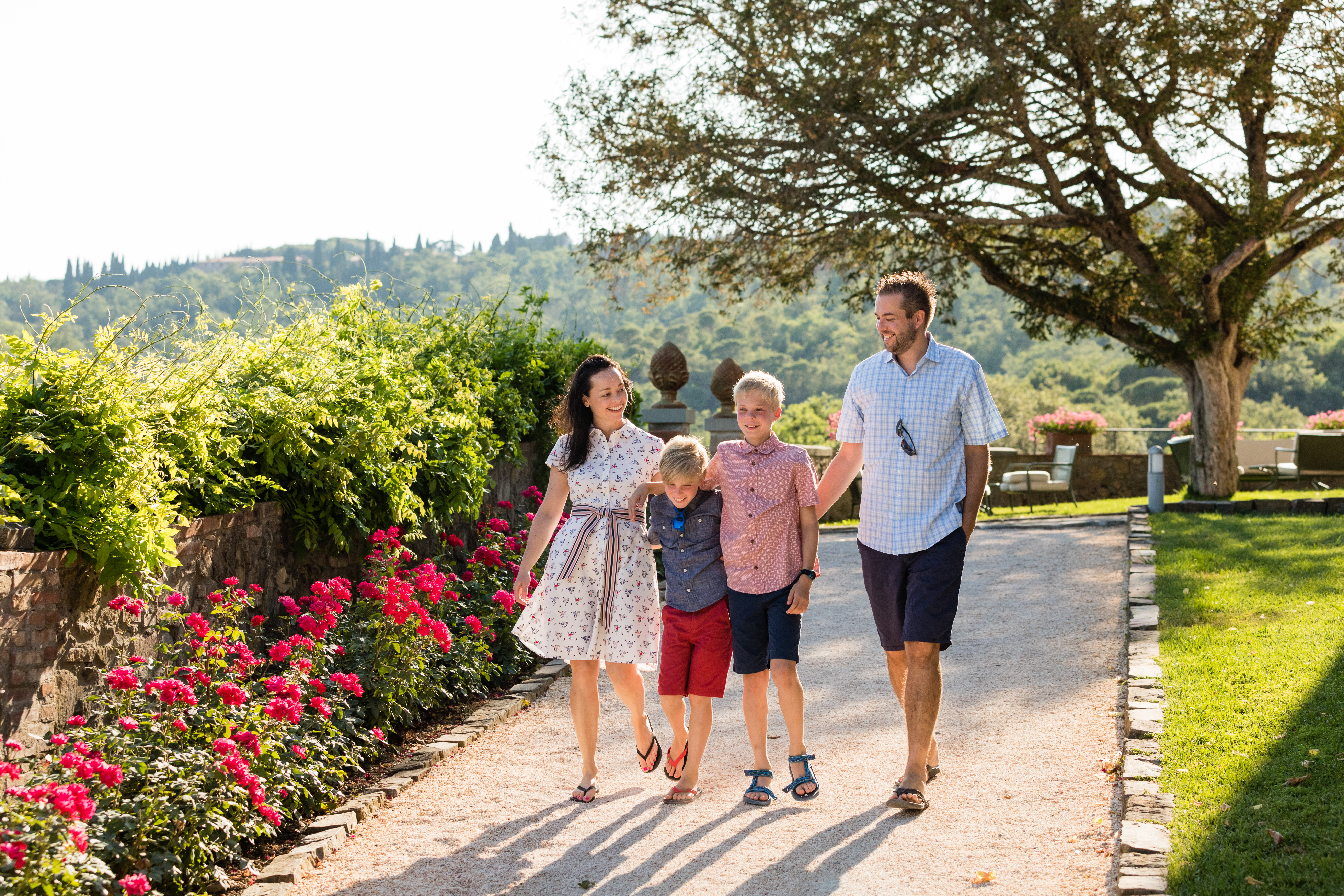 A family of four walks together on a garden path, smiling and holding hands.