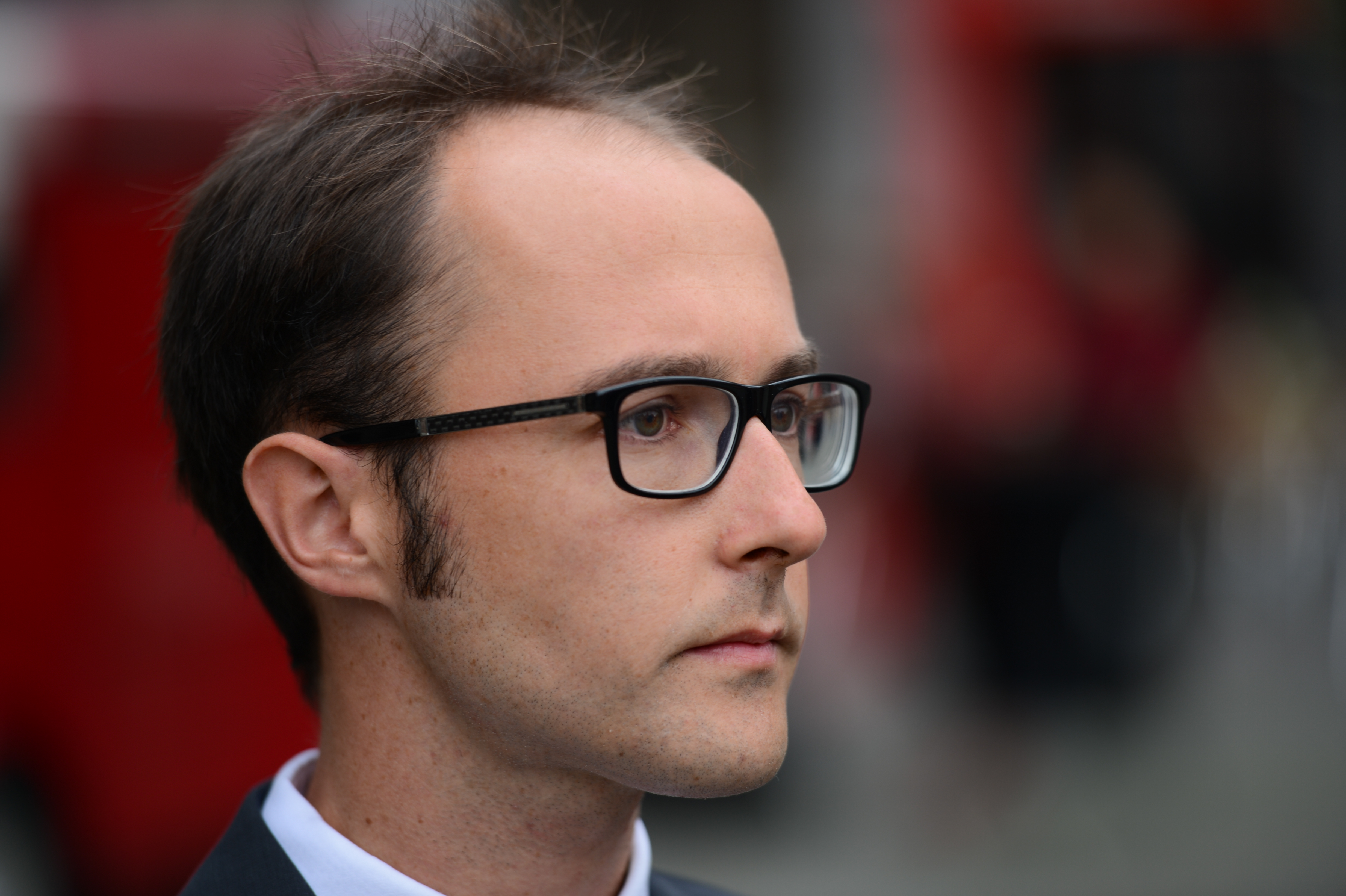 A man in glasses and a suit looks ahead with a serious expression during a wedding event.