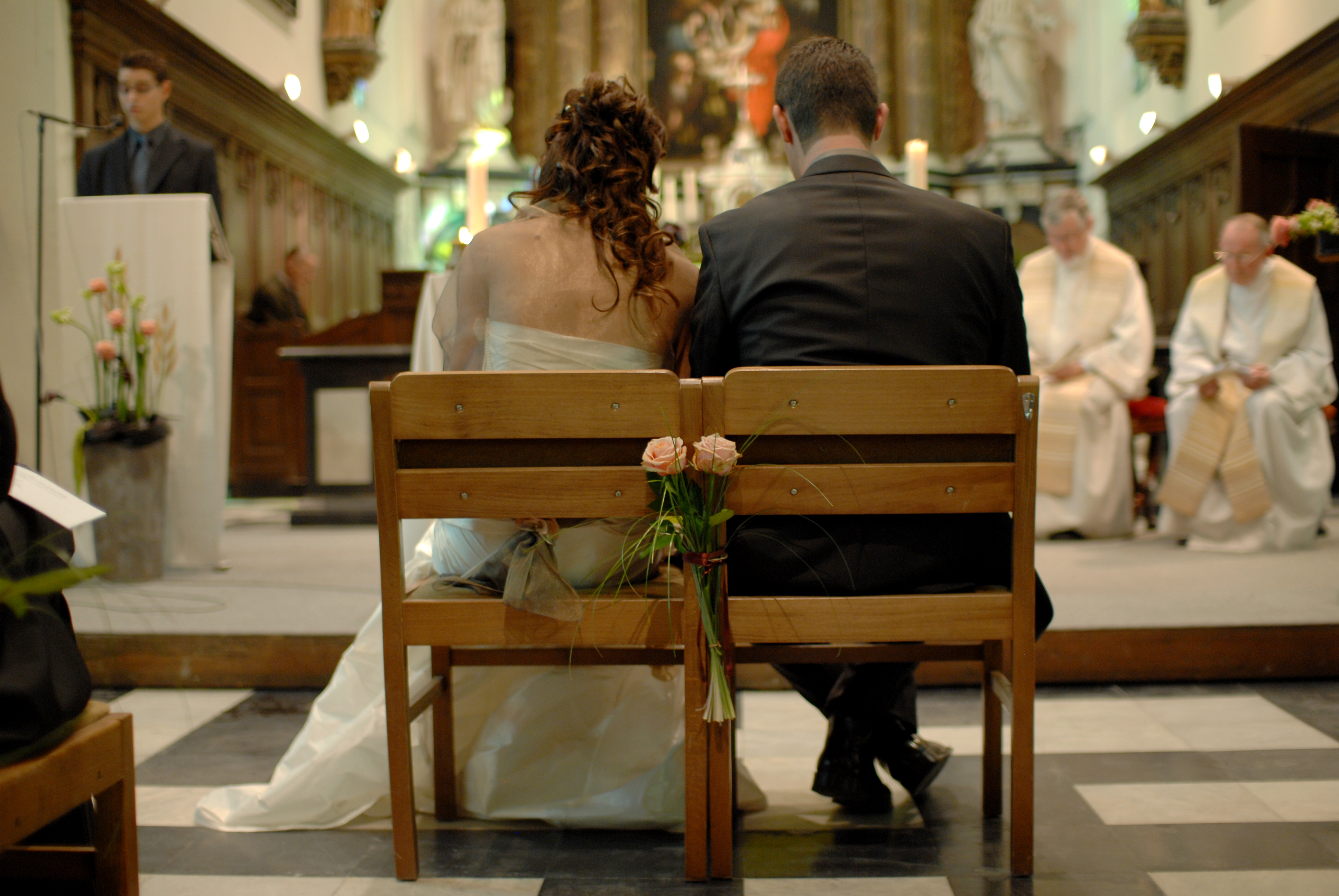A bride and groom sit side by side in a church during their wedding ceremony, facing the altar.