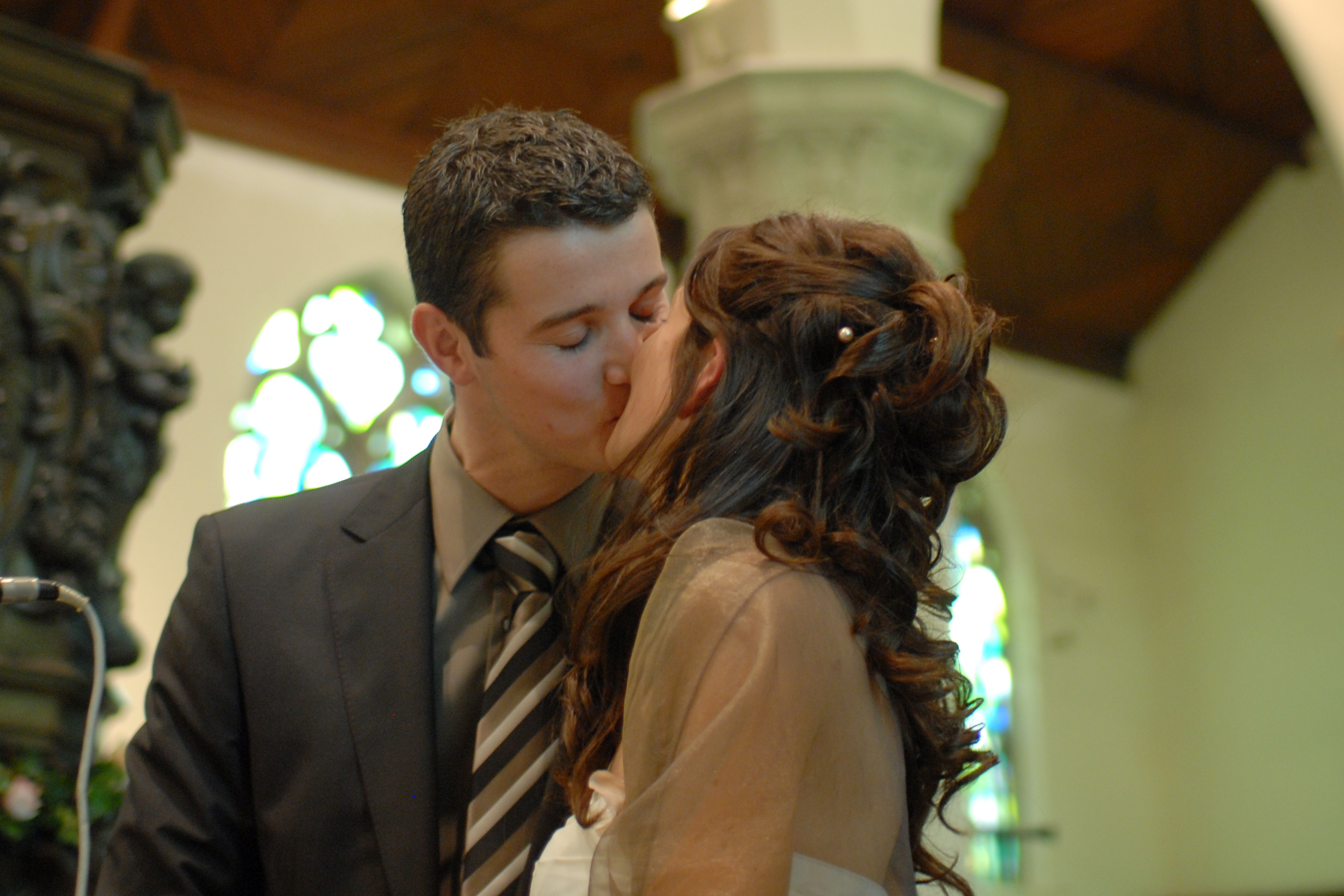 A bride and groom share a kiss during their wedding ceremony inside a church.