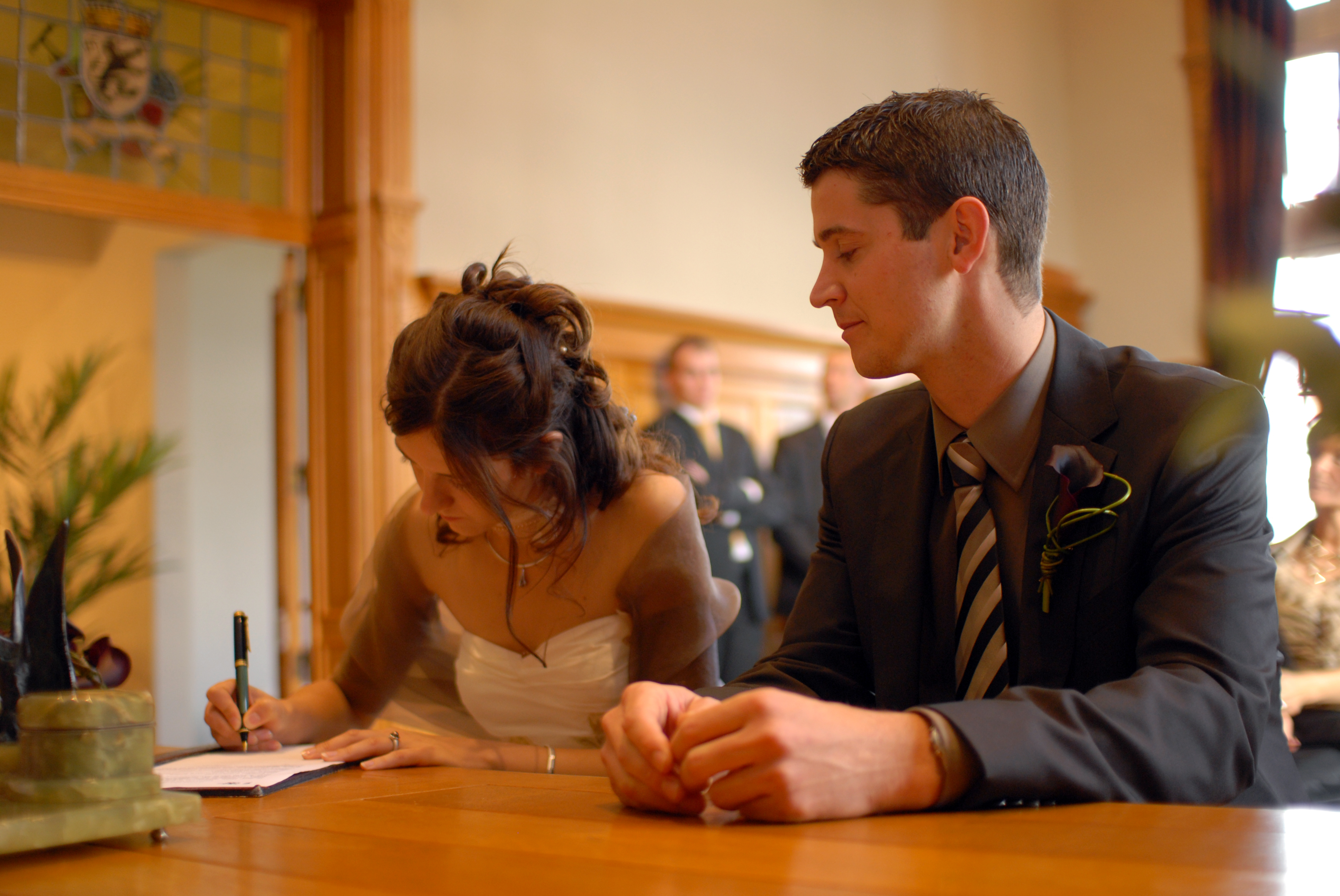 The bride signs a document while the groom sits beside her at a wedding ceremony.
