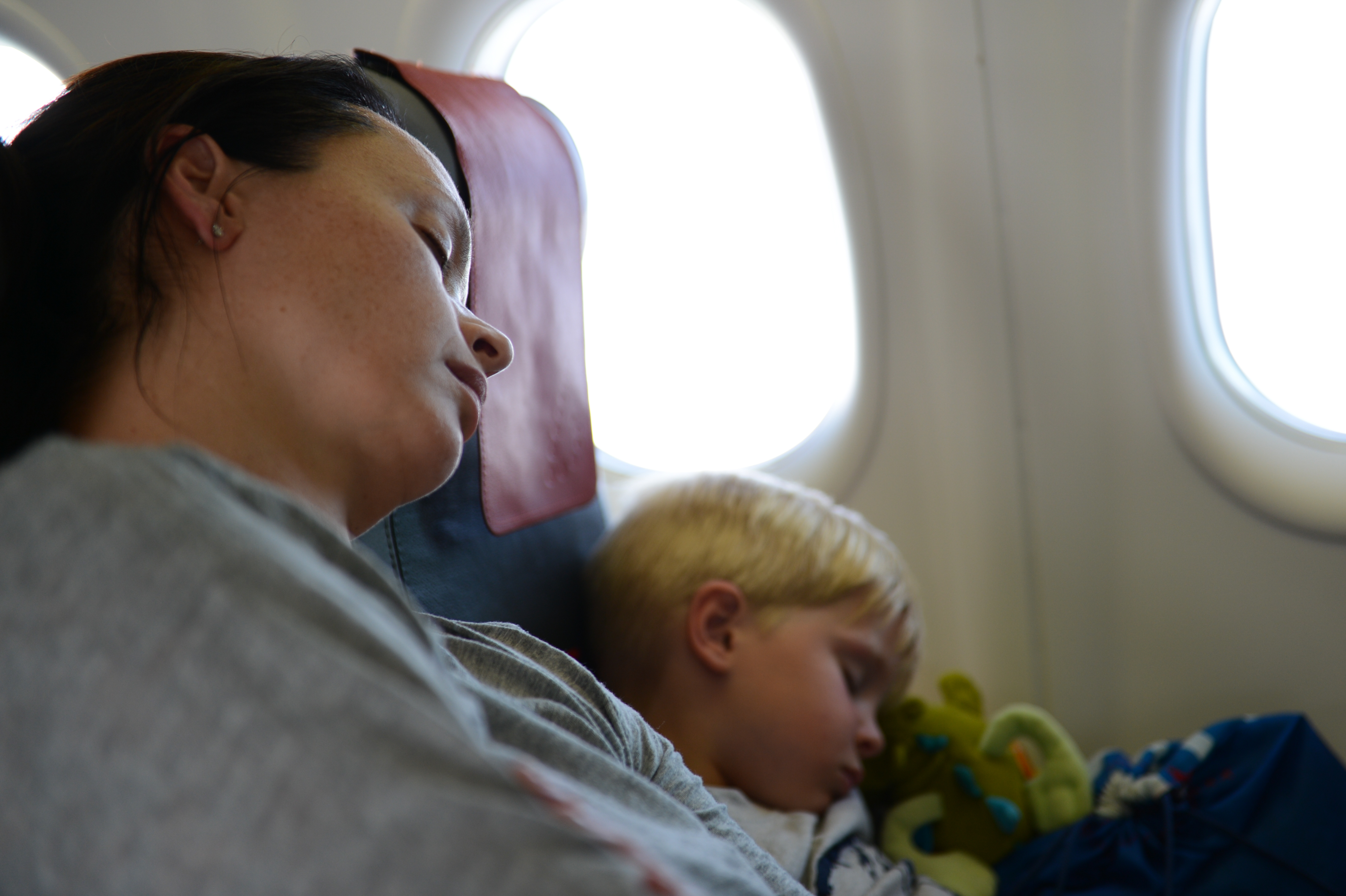 A woman and a young child sleep in their seats on an airplane, resting against each other.