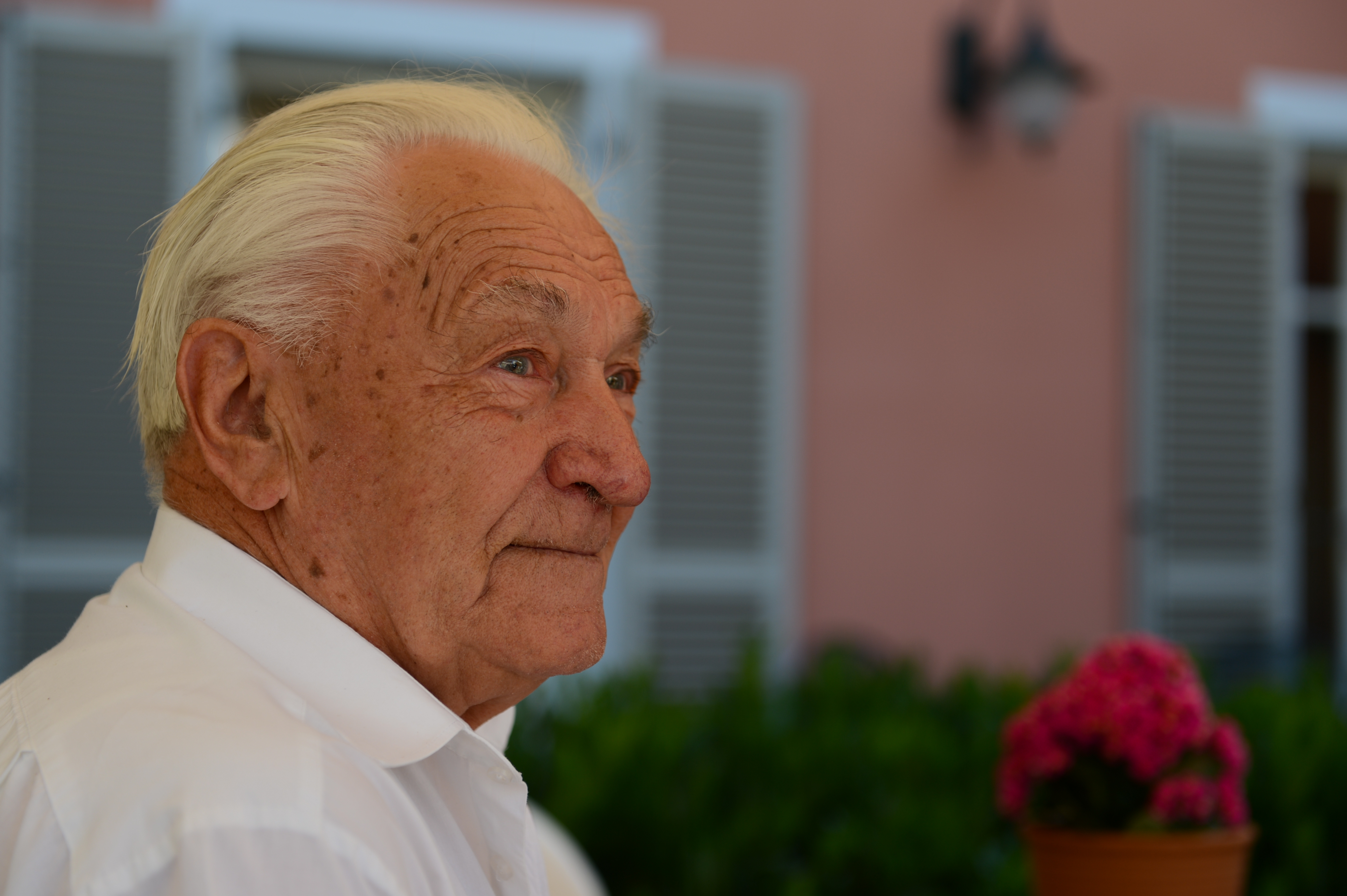 An elderly man in a white shirt looks off to the side at an outdoor wedding.