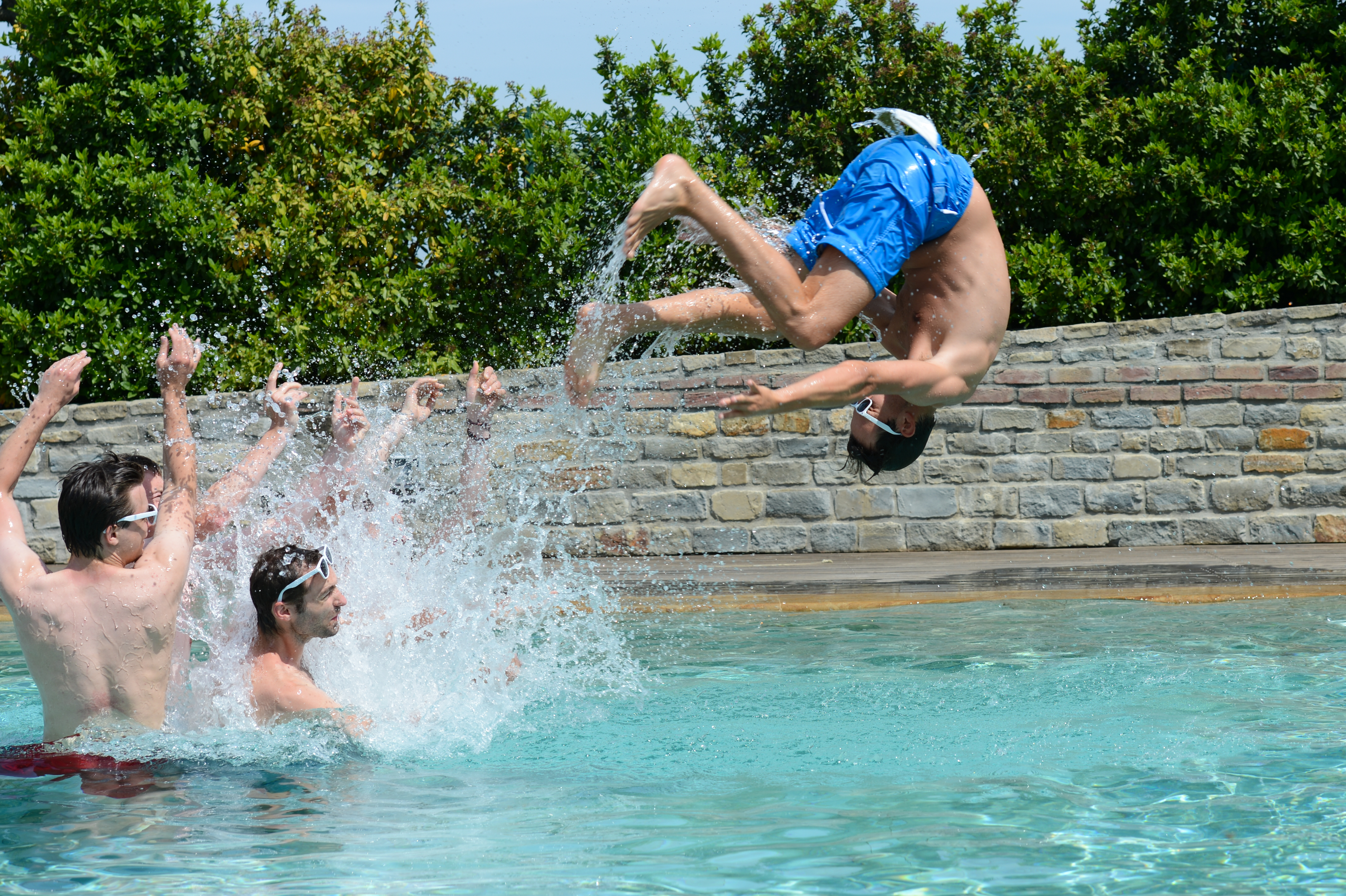 A group of men in a pool toss another man into the air as he flips backward.