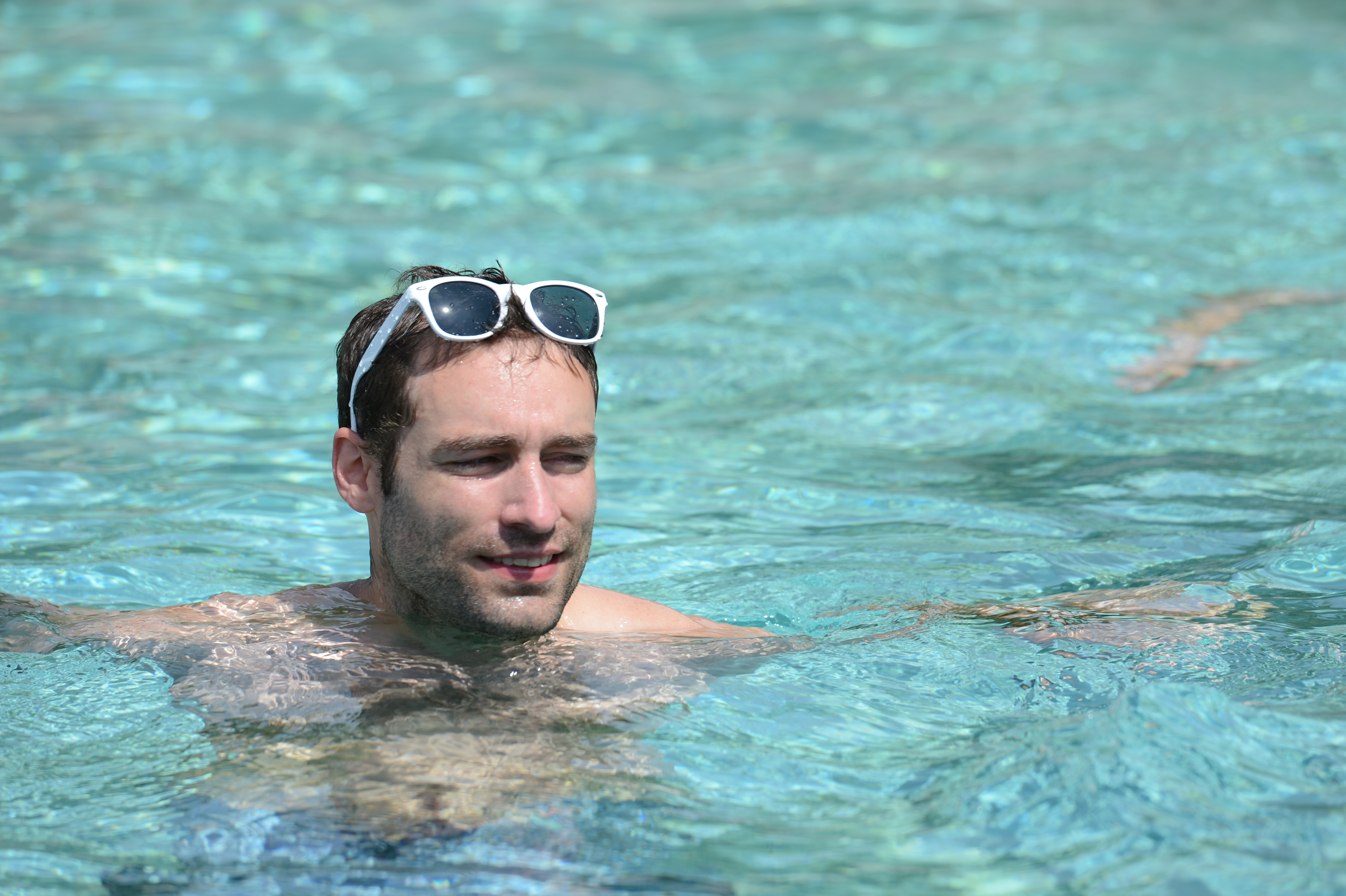 A man with sunglasses on his head is swimming in a pool, looking relaxed.