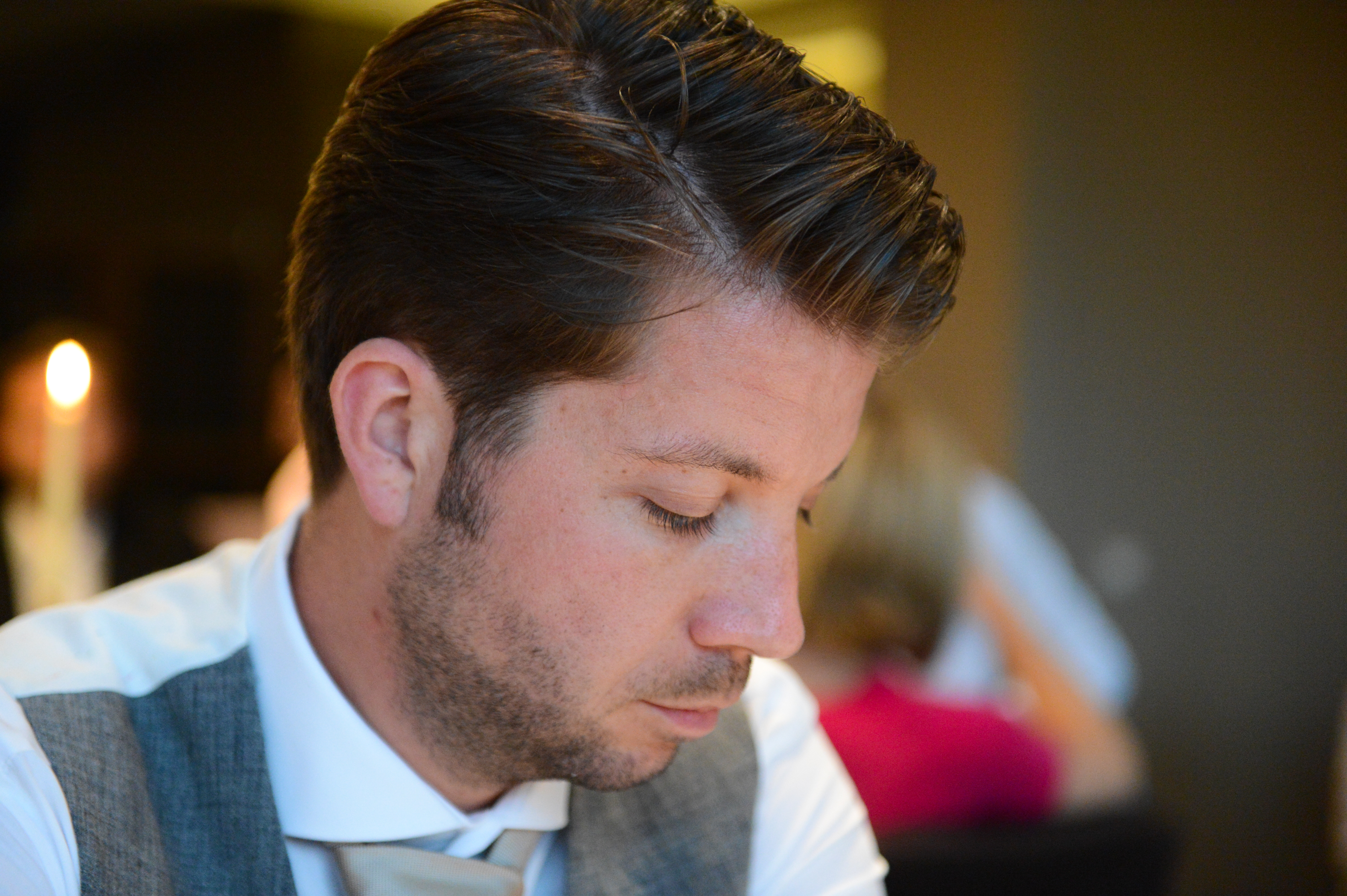 A man in formal wedding attire looks down with a thoughtful expression at a reception.
