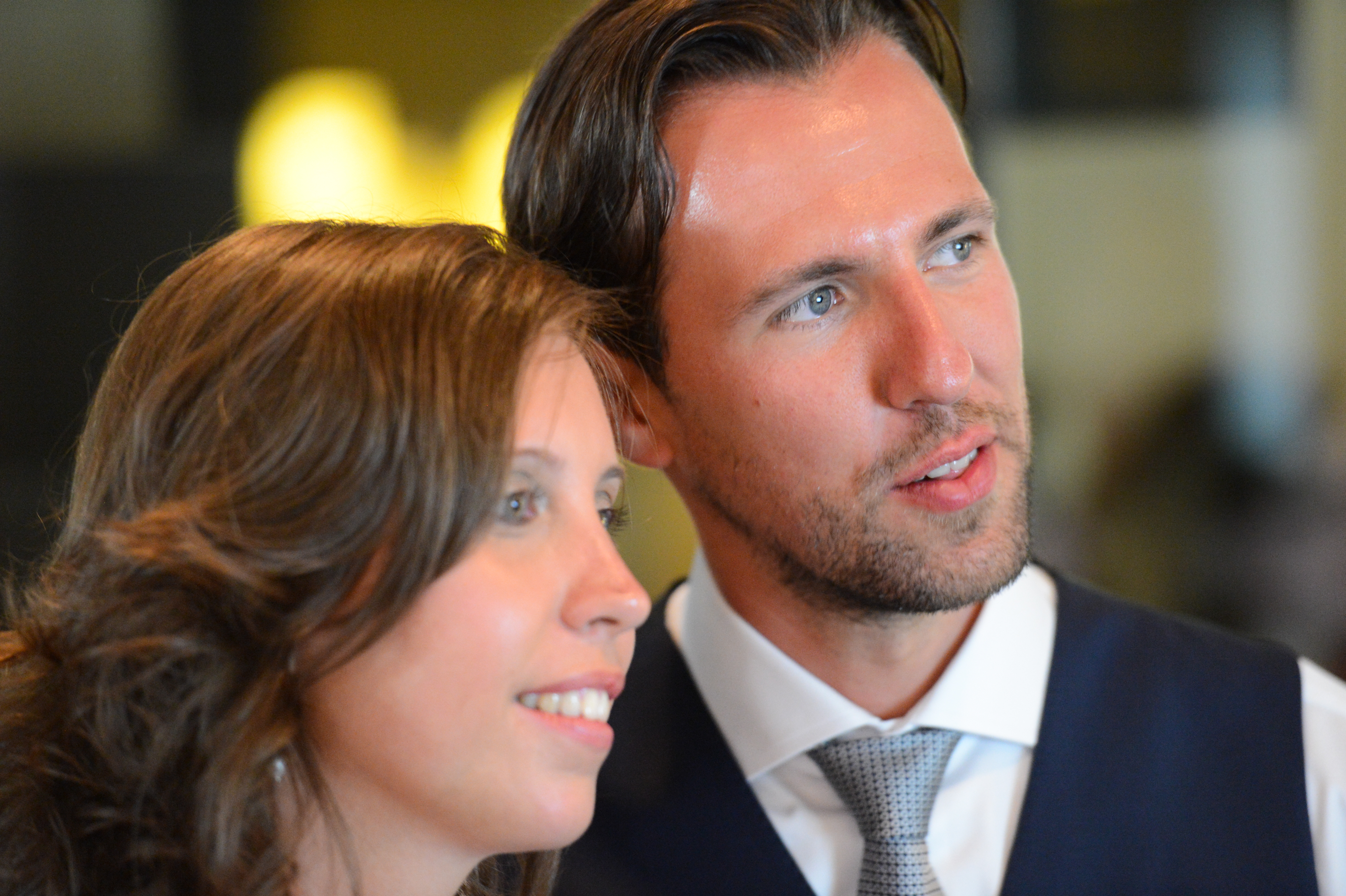 A bride and groom stand close together, smiling and looking in the same direction during their wedding.
