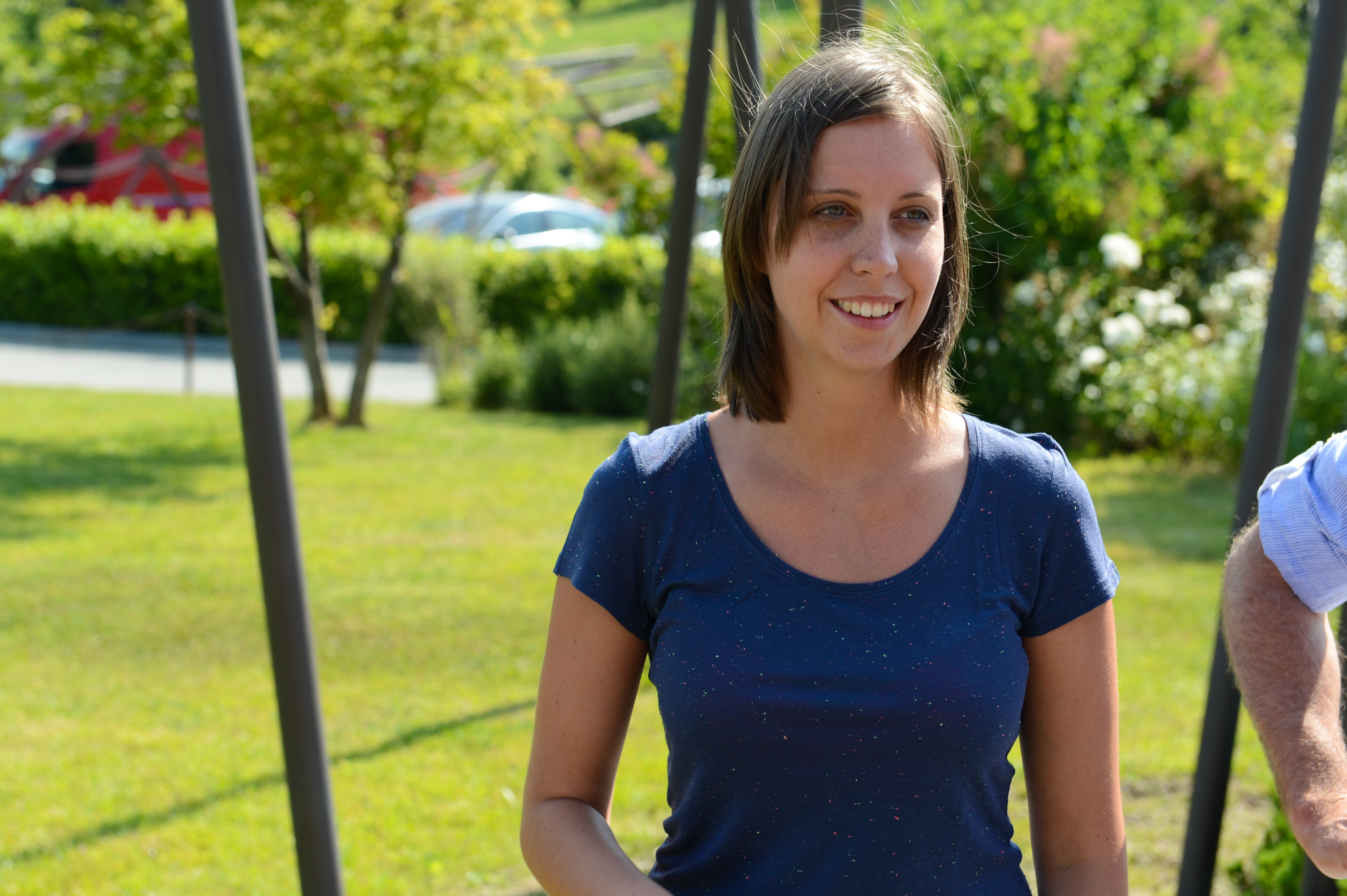 A woman in a blue shirt smiles while standing outdoors at a wedding event.